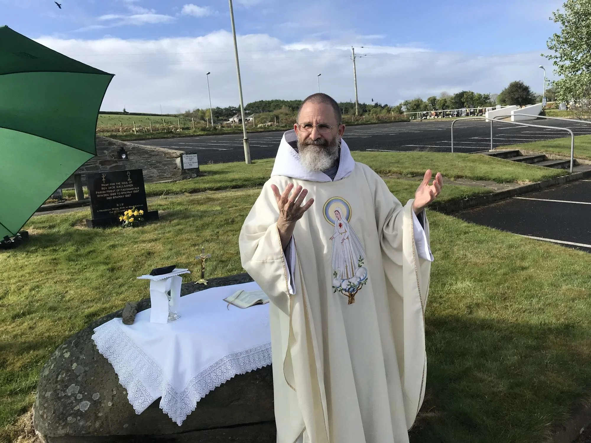 A Franciscan friar prays with open hands at an outdoor altar