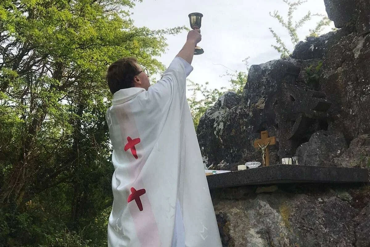 Fr Fergal Cummins raises a chalice at Clara Mass Rock
