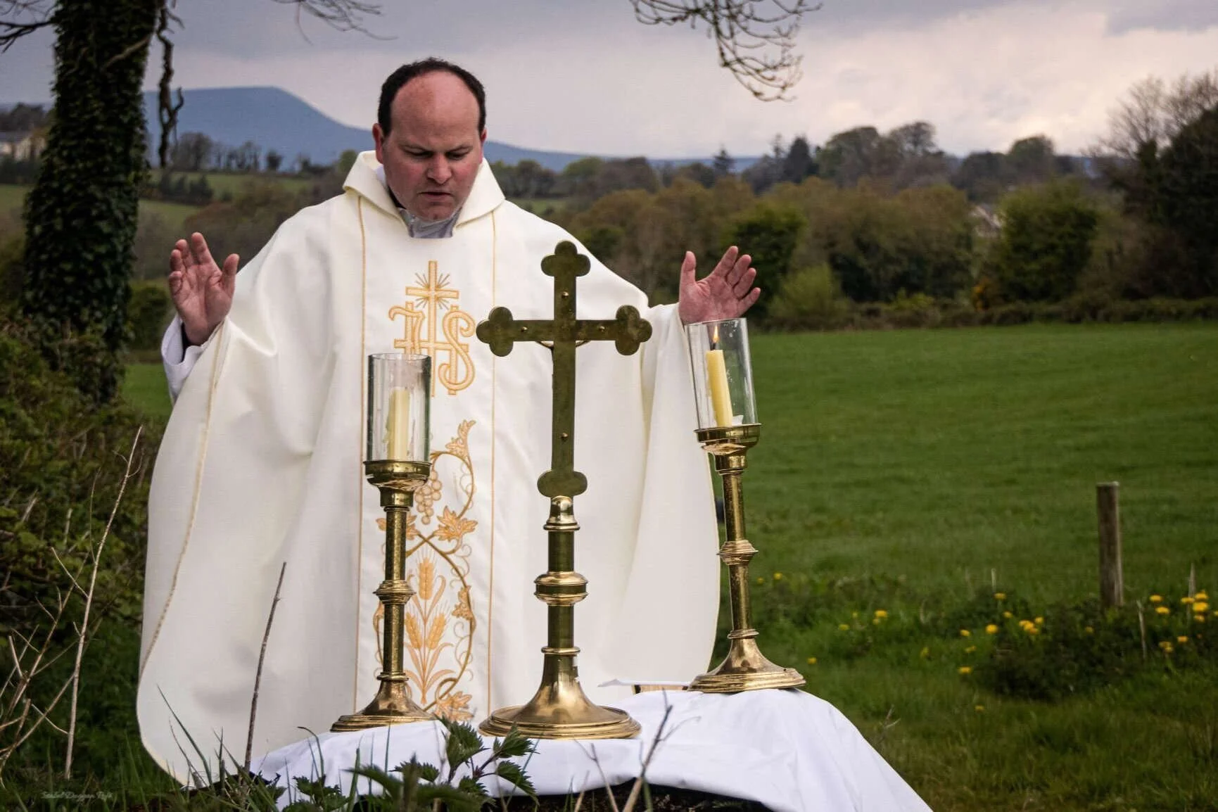 Fr Sean Maguire prays with open hands at a Mass Rock in Kilmore