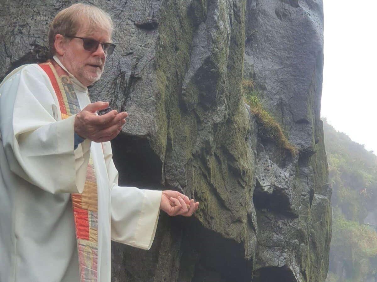 A priest prays beside a rock face during outdoor Mass