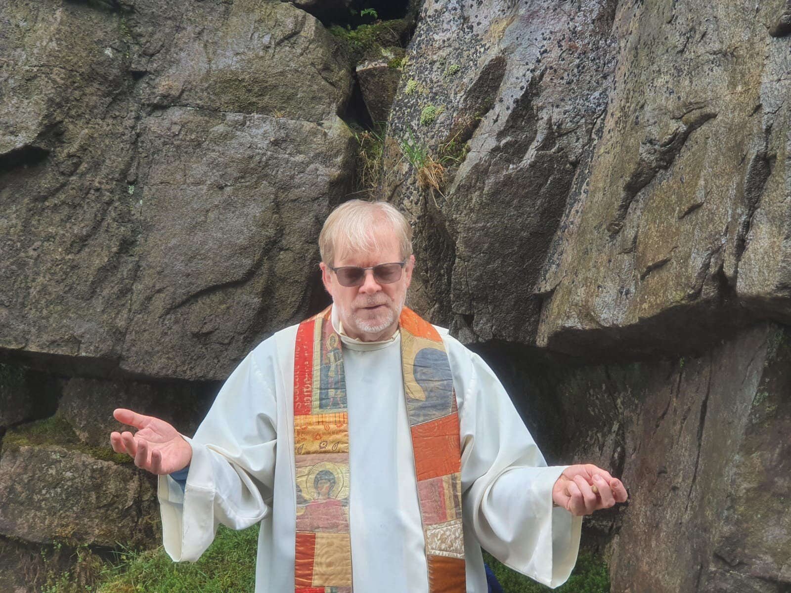 A priest addresses worshippers beside a rocky outcrop