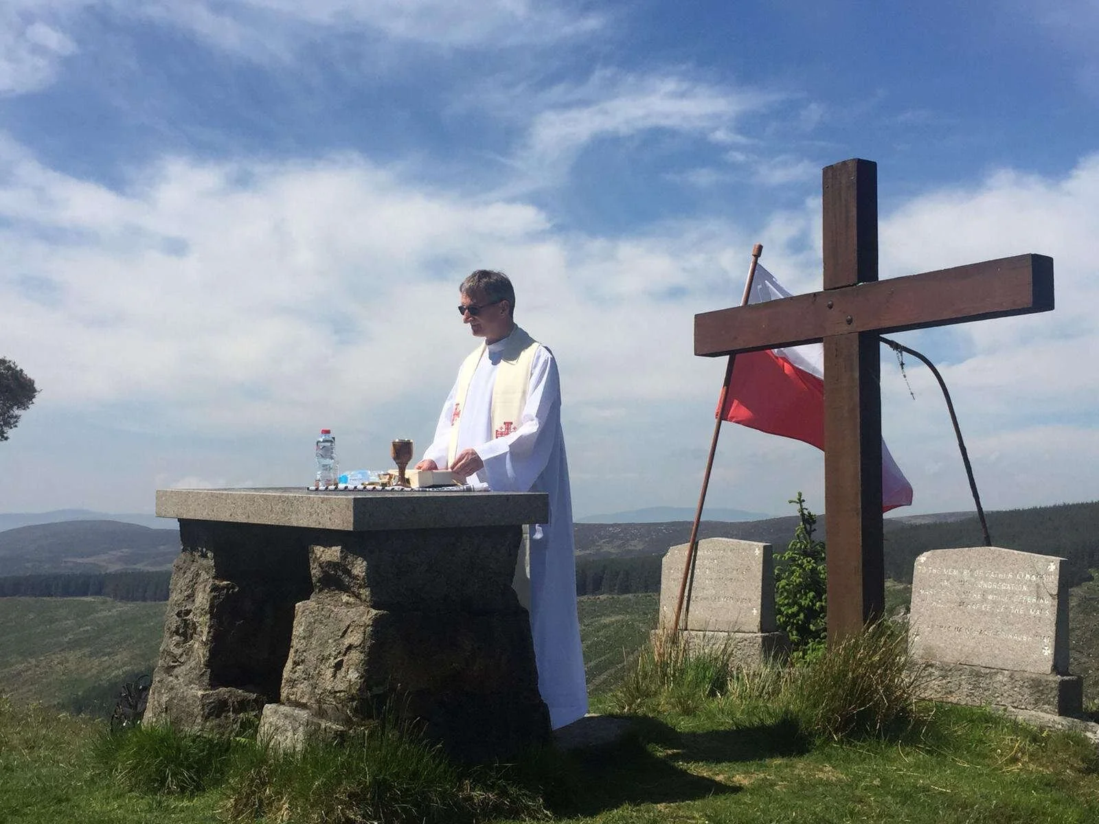A priest celebrates Mass at a hilltop altar beside a wooden cross
