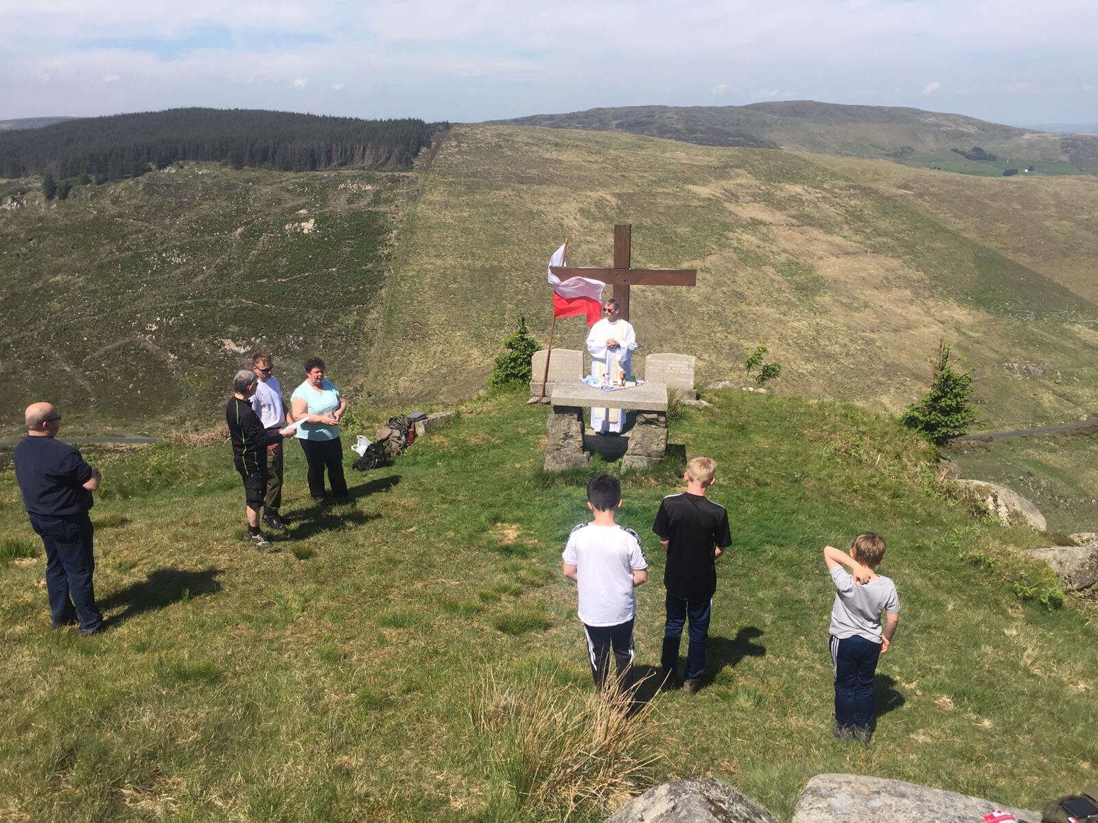 Worshippers gather at a hilltop Mass Rock beside a wooden cross