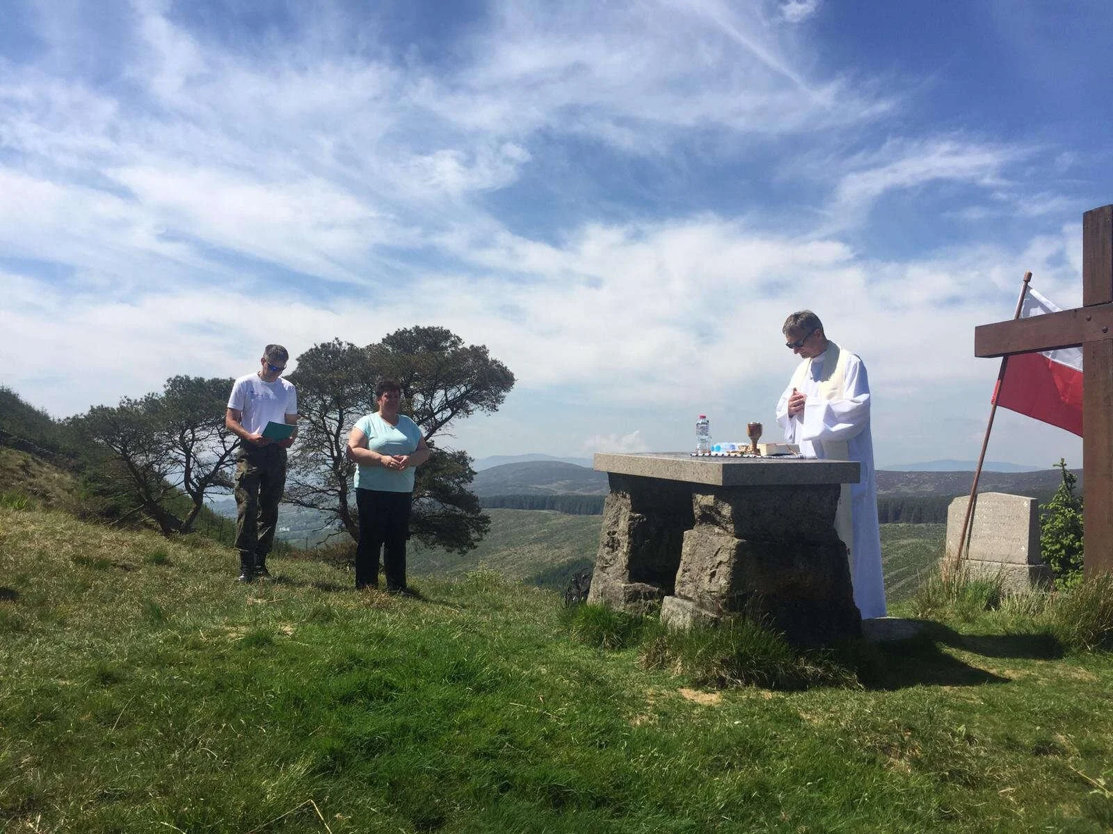Worshippers stand beside a priest at a hilltop Mass Rock