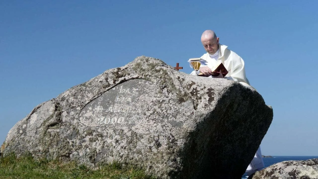 A priest celebrates Mass behind a large coastal boulder