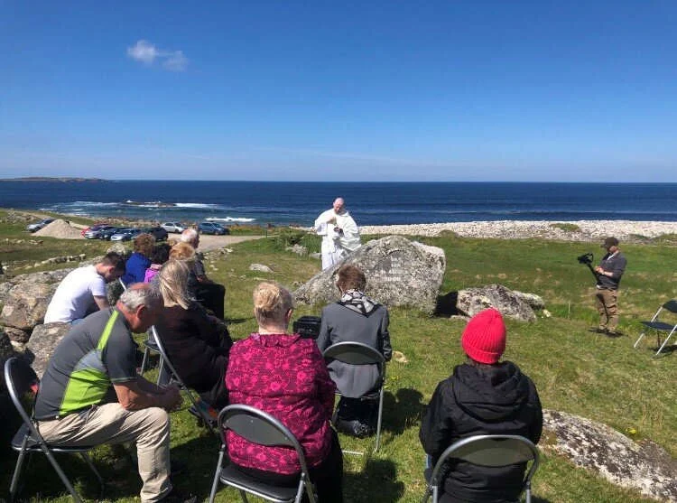 Worshippers sit on coastal grass during Mass at a rock altar