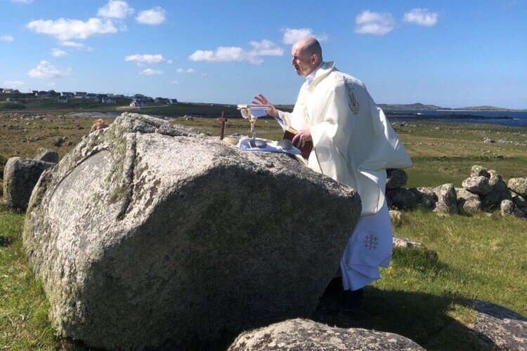A priest reads from a missal at a coastal Mass Rock
