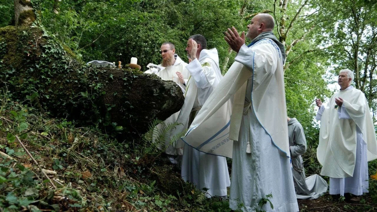 Priests celebrate Mass at a stone altar in woodland
