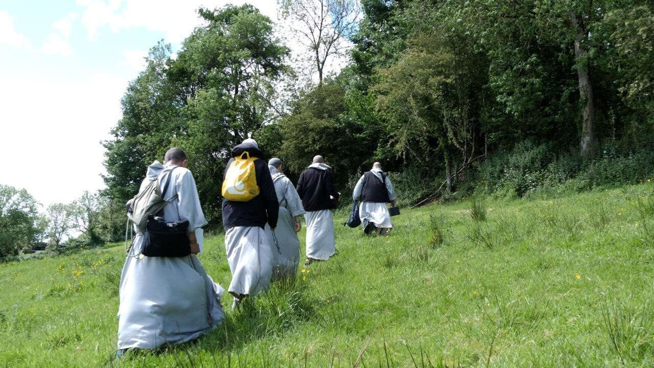Priests walk across grass towards a woodland Mass Rock