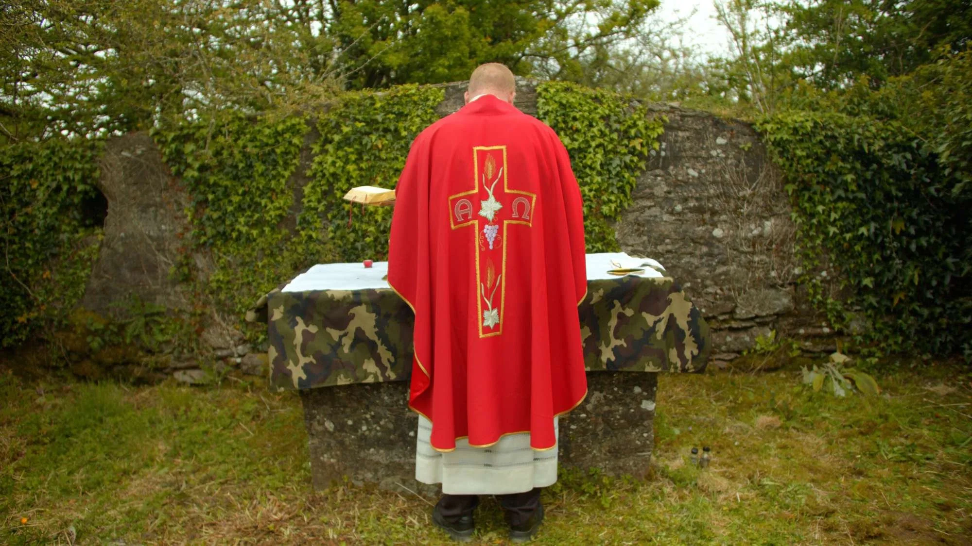 A priest faces a stone altar during outdoor Mass
