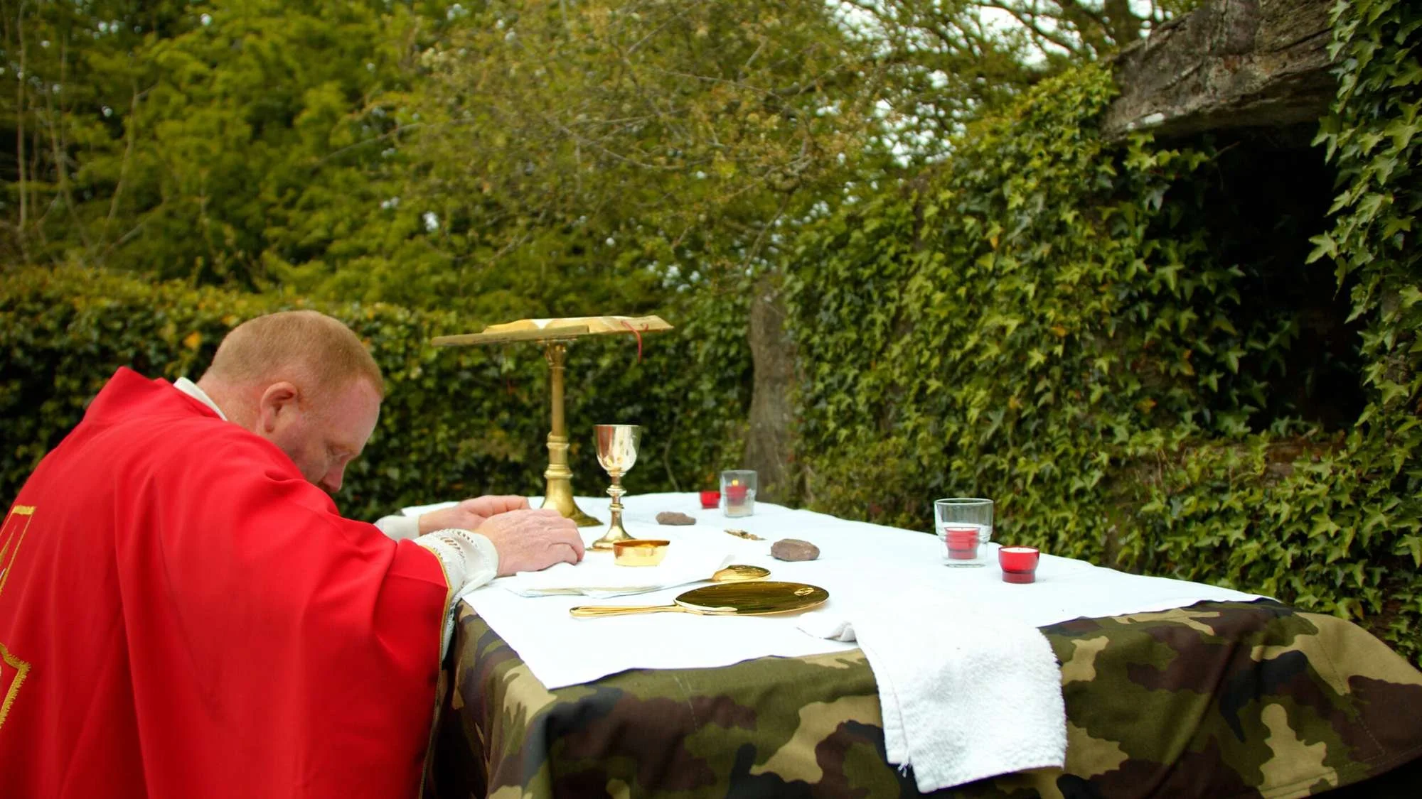A priest bows over a woodland Mass Rock altar