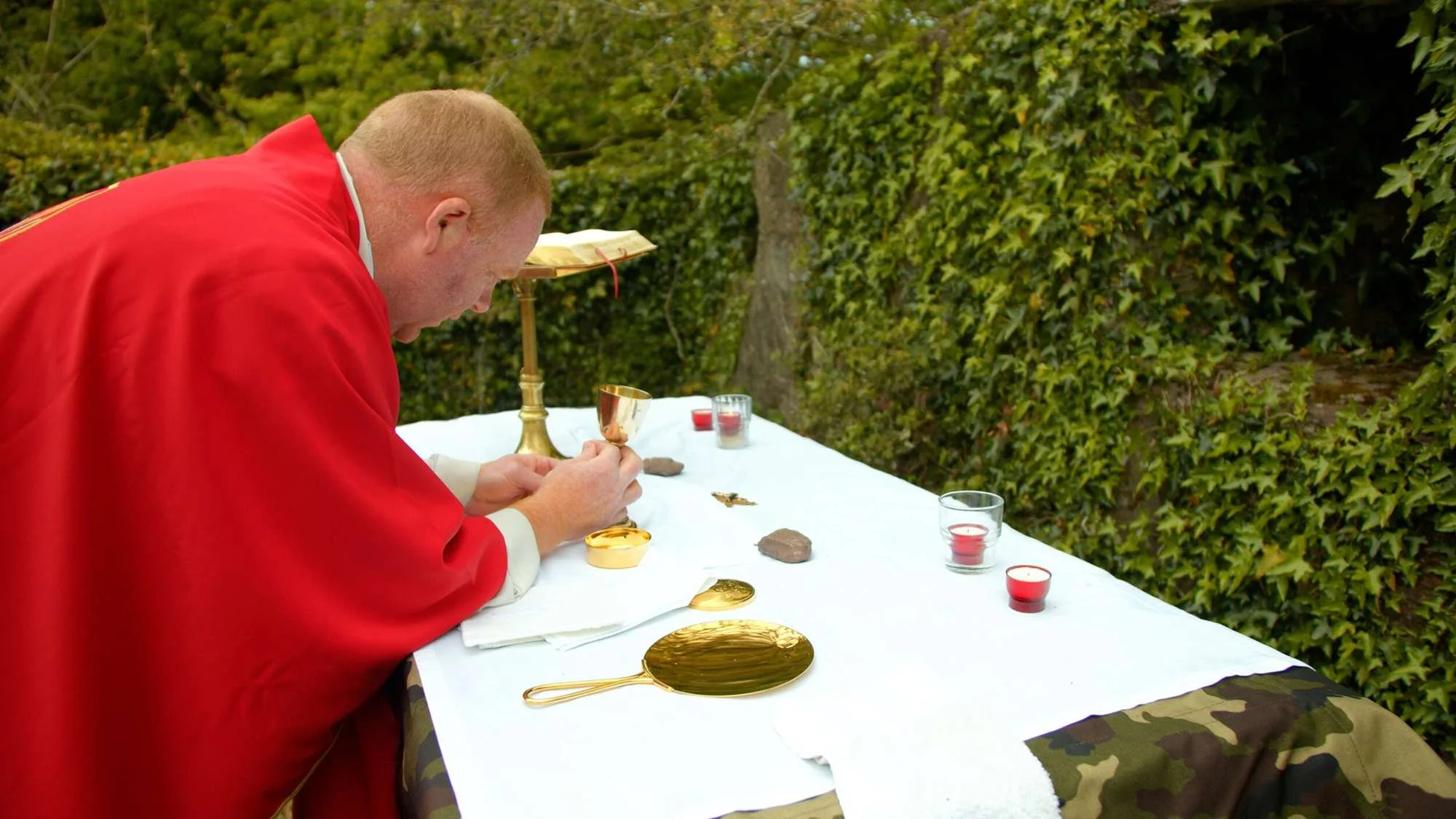 A priest reads from a missal at a woodland altar