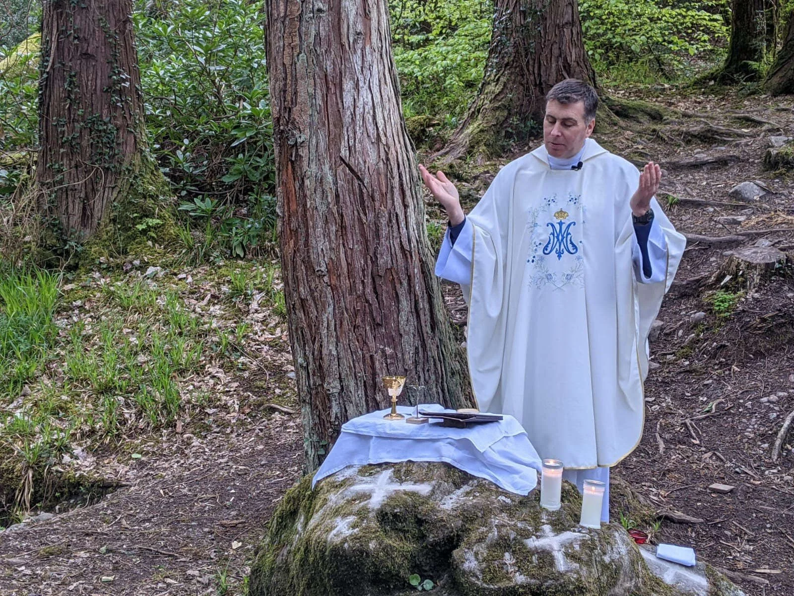 A priest prays beside a tree at Pike Wood Mass Rock