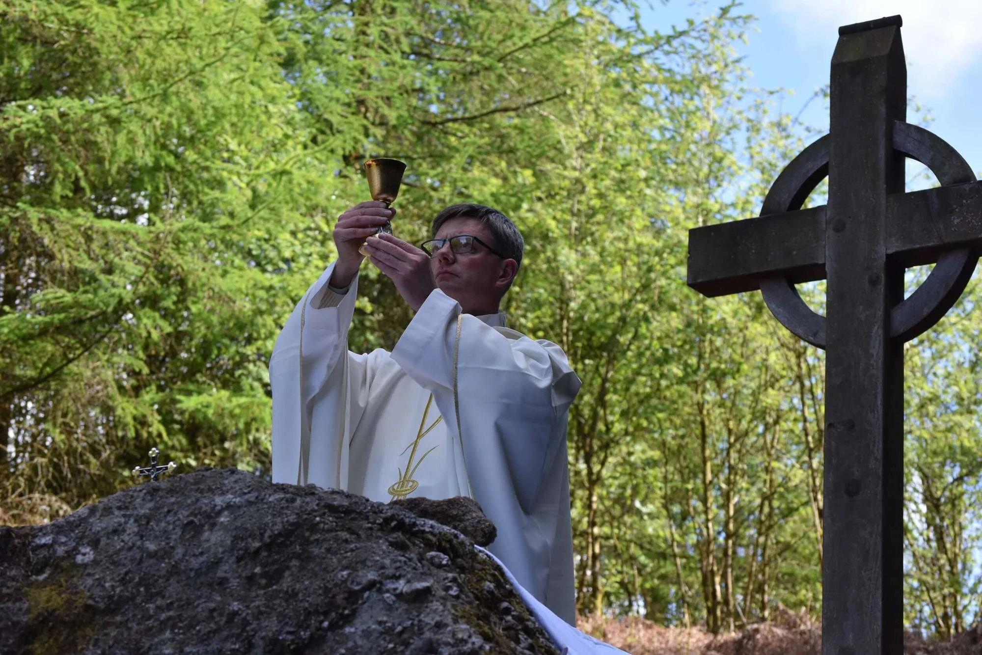 Fr Patrick Cahill raises a chalice beside a woodland cross