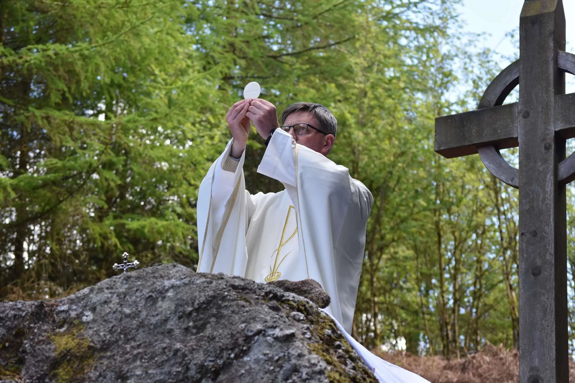 Fr Patrick Cahill elevates the host beside a stone Celtic cross