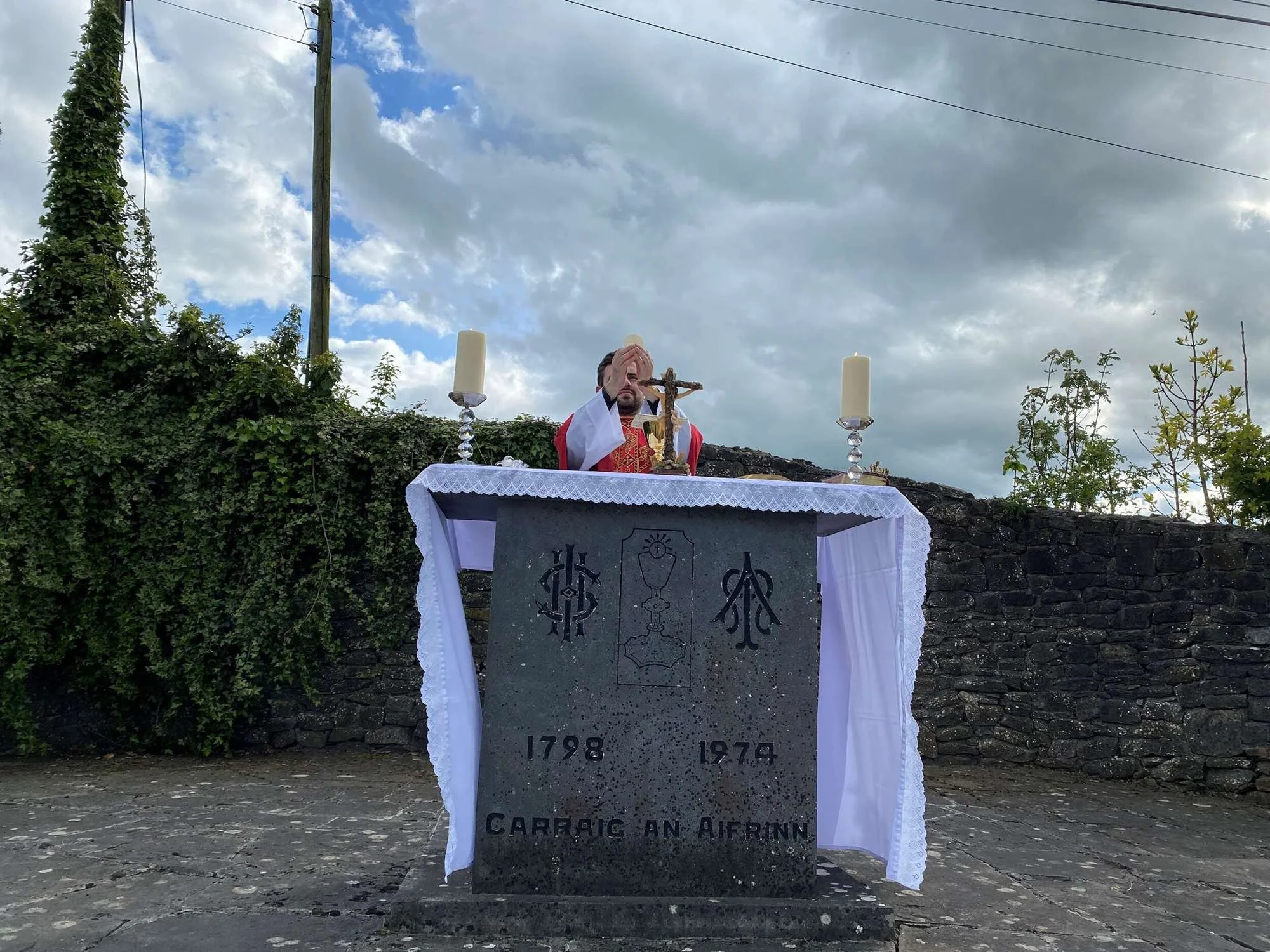 A priest bows behind a stone altar during outdoor Mass