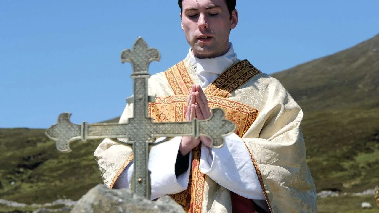 A priest holds the host beside a stone cross