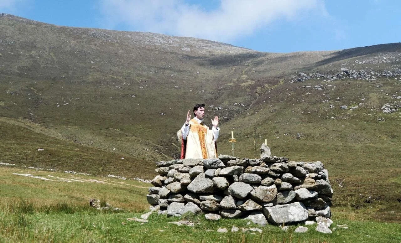 A priest stands behind a circular stone altar on a hillside