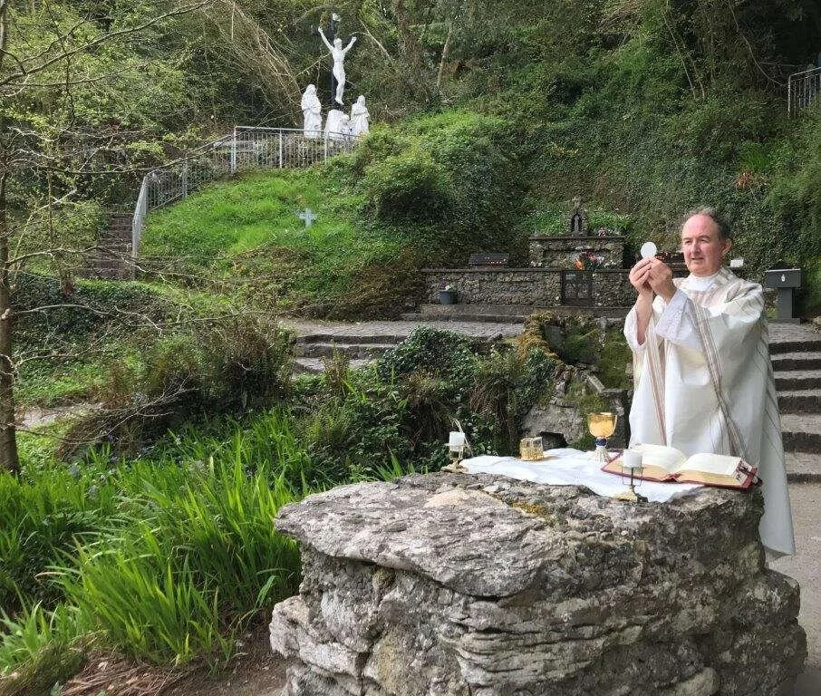 Fr Jim Murray prays at a stone altar below a hillside statue