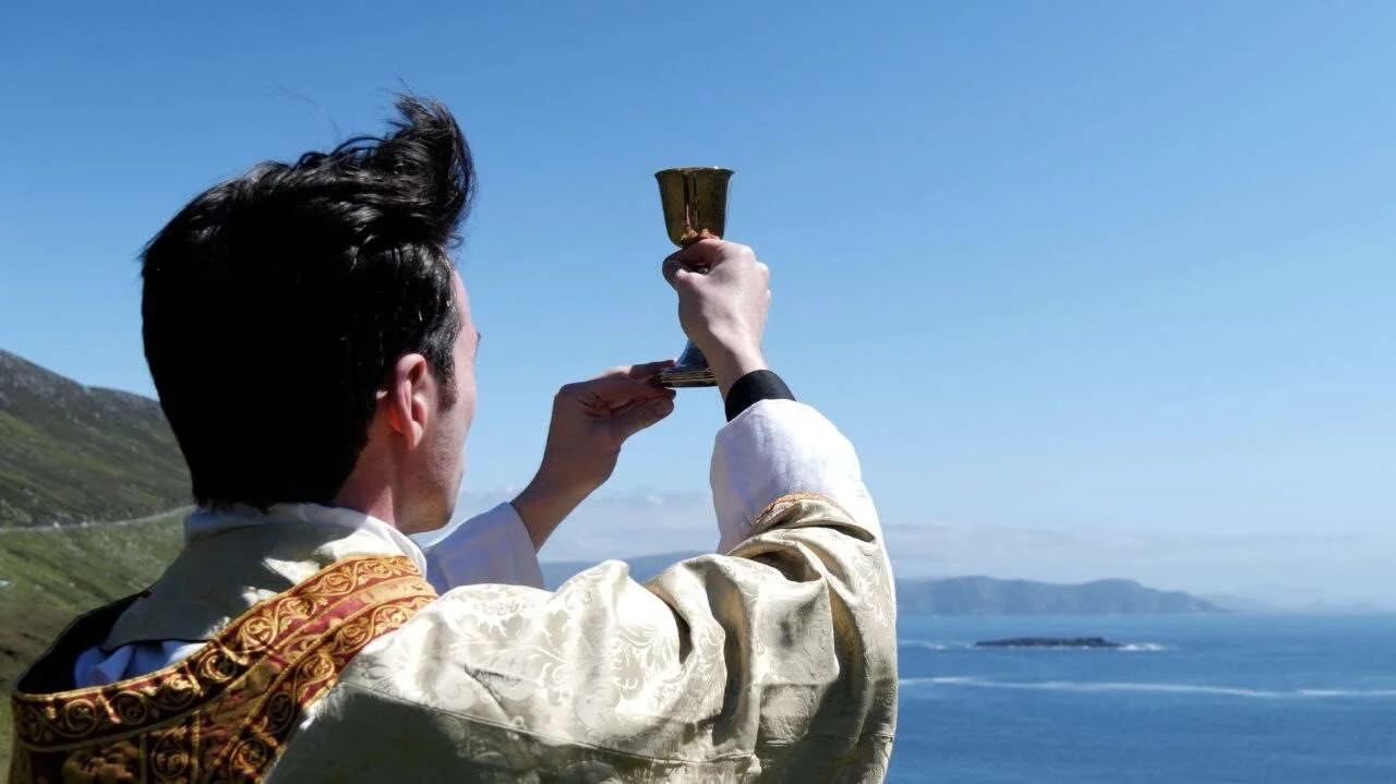 A priest raises a chalice overlooking the sea in Tuam