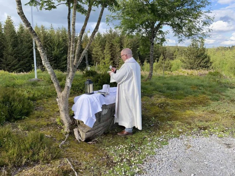 A priest celebrates Mass at a rock altar beside a tree