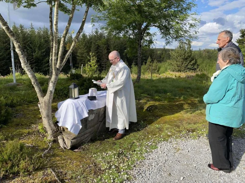 Worshippers stand beside a priest celebrating outdoor Mass