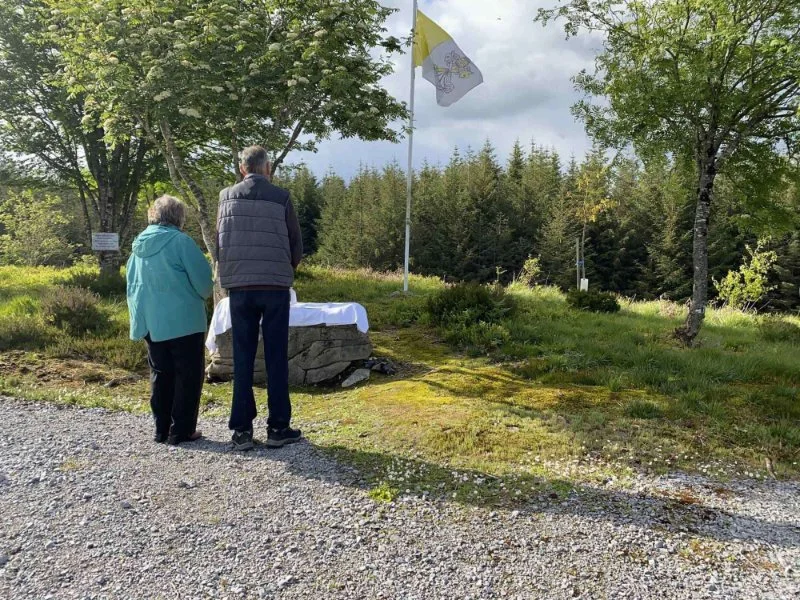Worshippers stand beside a rock altar in a grassy clearing