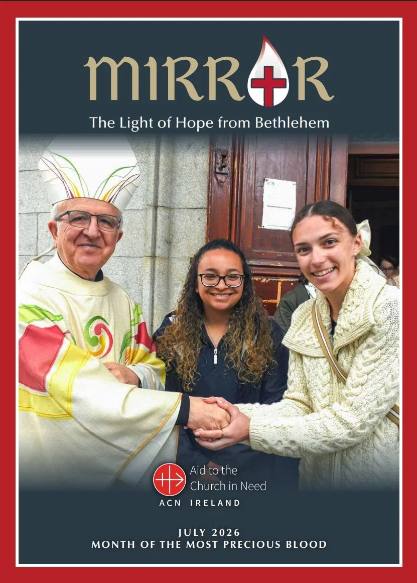 A bishop stands beside two smiling young women shaking hands for Mirror Magazine July 2026 Issue in front of a church doorway.