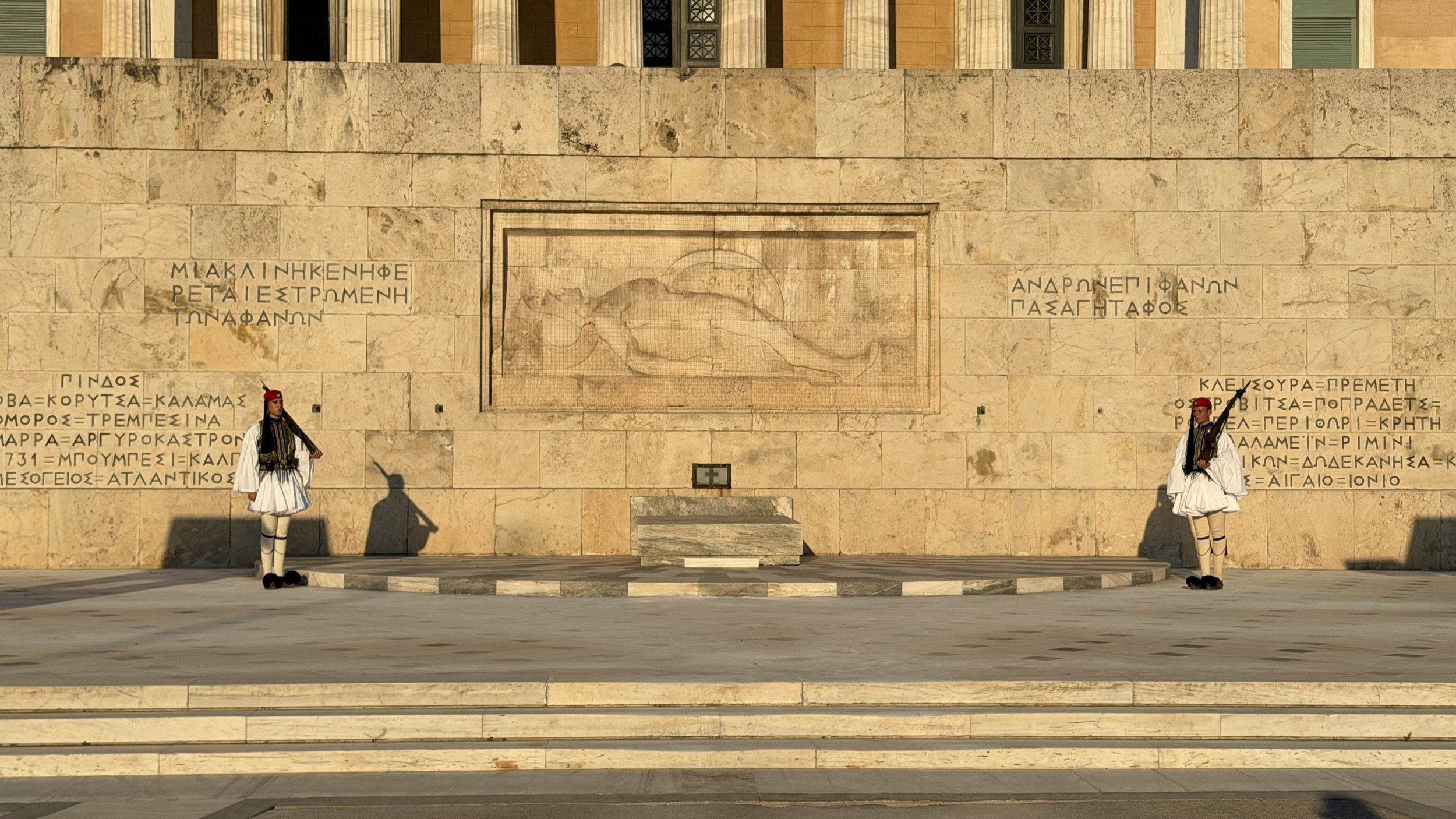 Evzones standing guard at the Tomb of the Unknown Soldier in Syntagma Square, Athens, illuminated by golden hour sunlight.