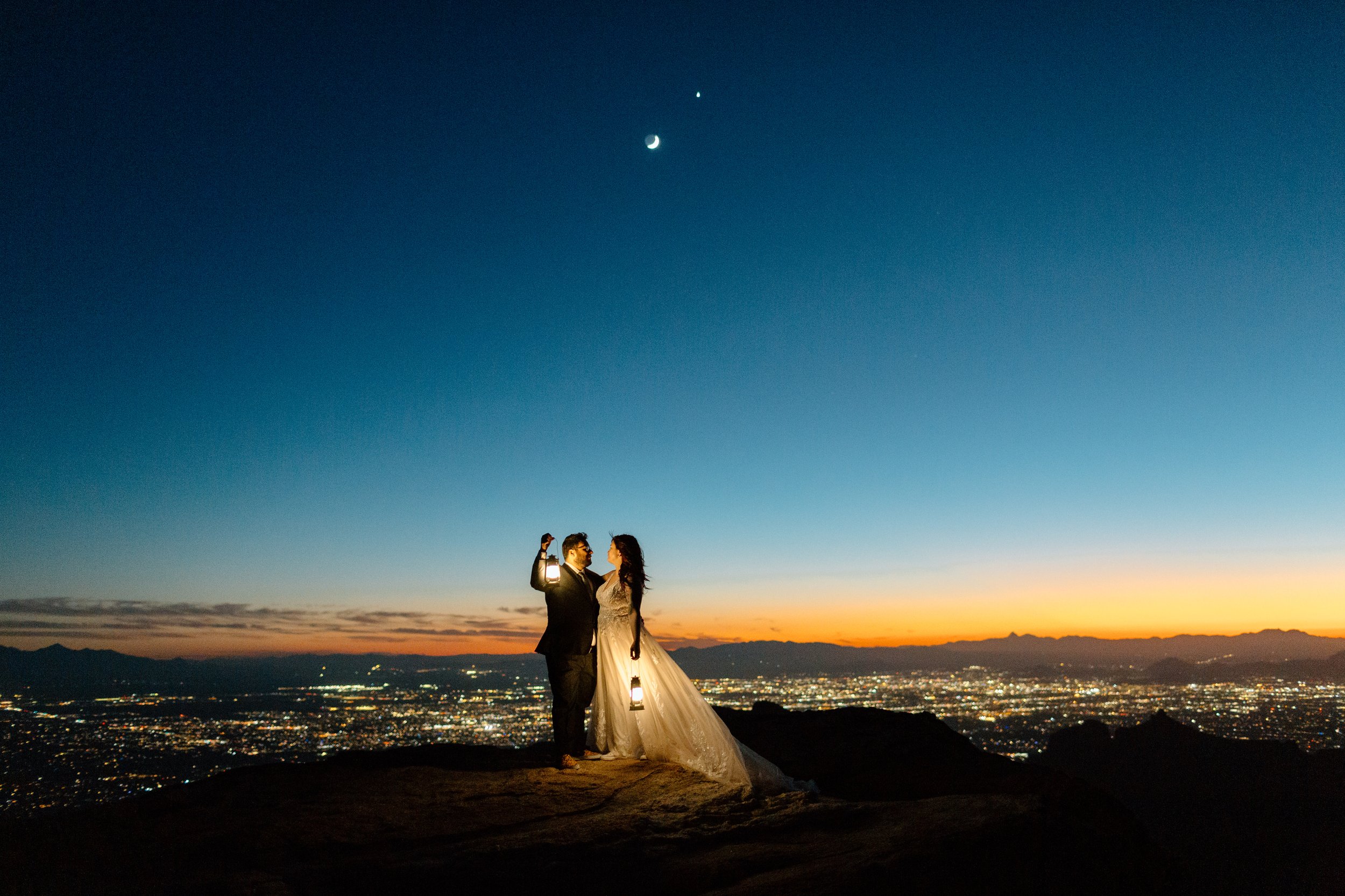 elopement couple stand together and hold lanterns above the city of Tucson at dusk