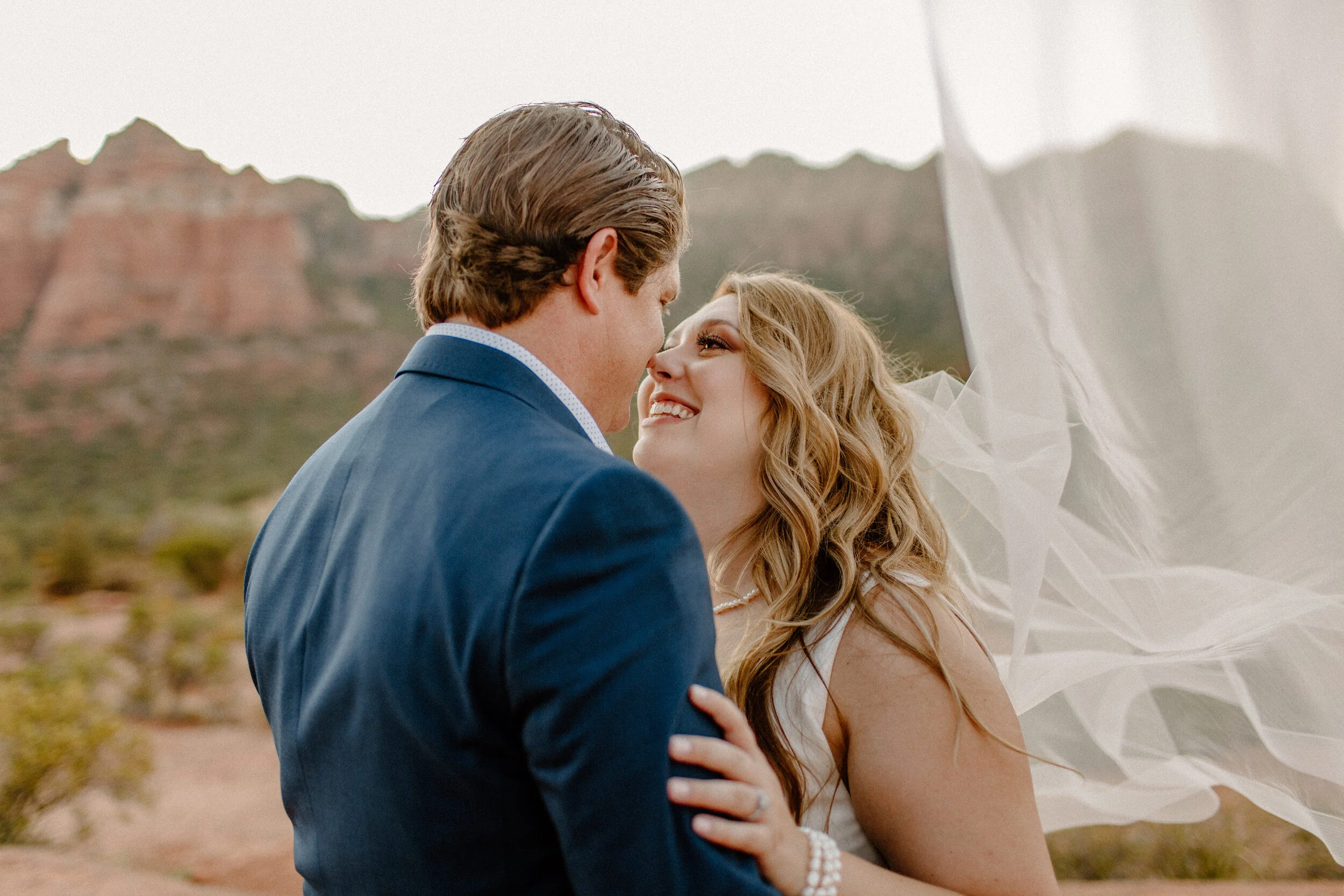 elopement couple share a hug while bride’s veil flies back in sedona arizona, sedona elopement photographer, lucy b. photogrpahy
