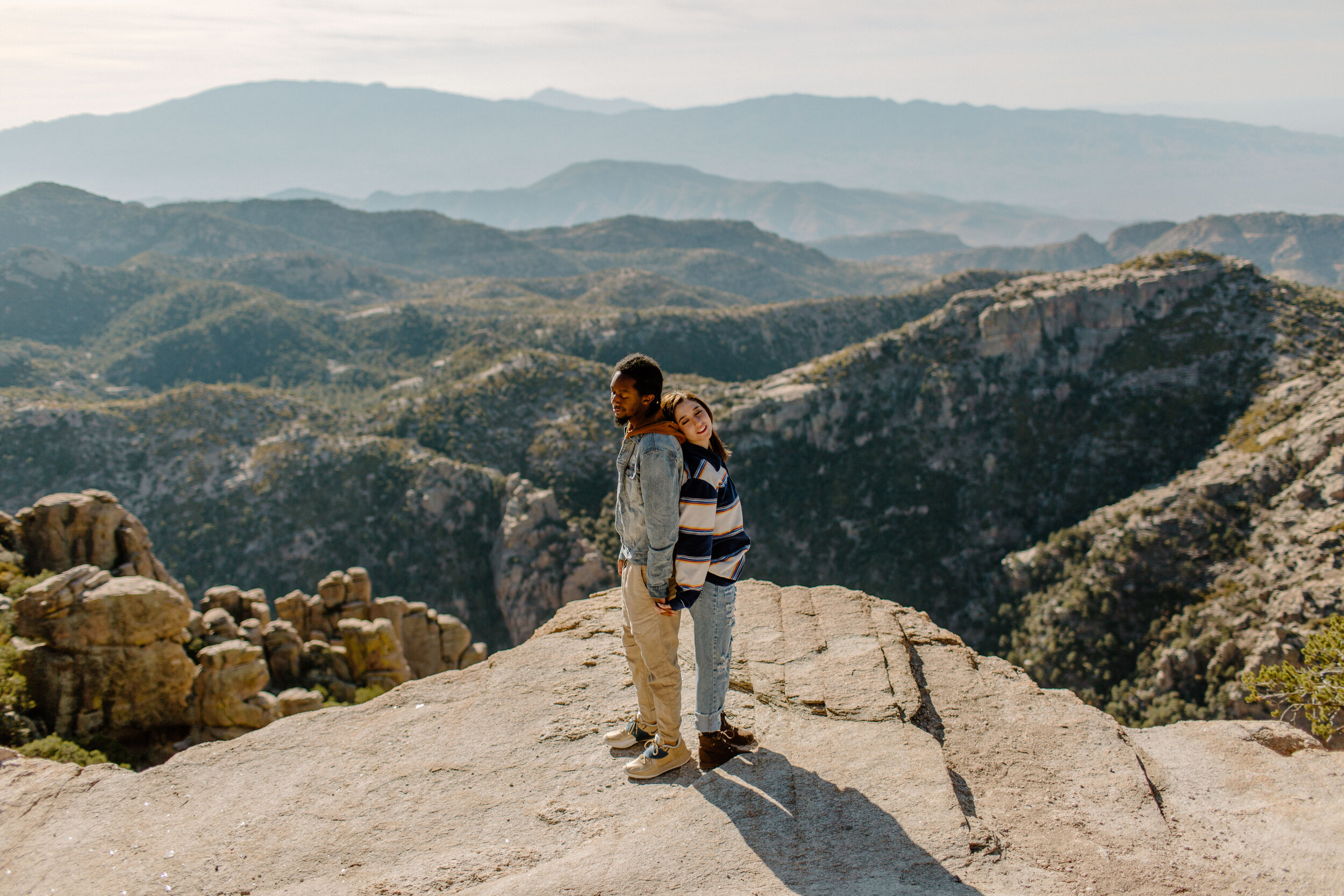  Couple stands back to back in front of a mountain view at Windy Point on Mount Lemmon in Tucson Arizona. Arizona couples photographer, Lucy B. Photography. 