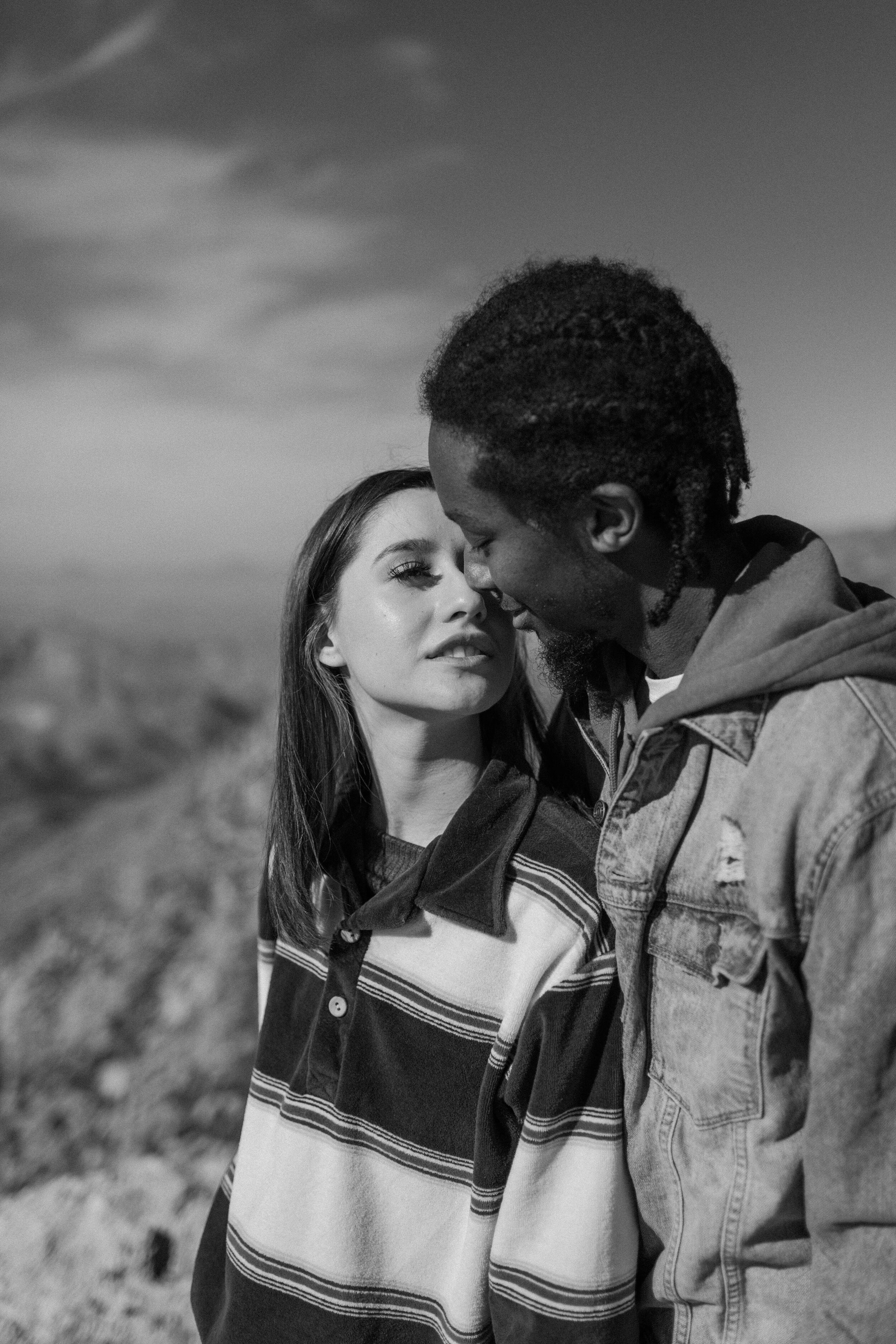  Black and white photo of a couple kissing. Woman stands in front of her boyfriend and turns her head to kiss him at Windy Point on Mount Lemmon in Tucson Arizona. Tucson couples session, Lucy B. Photography. 