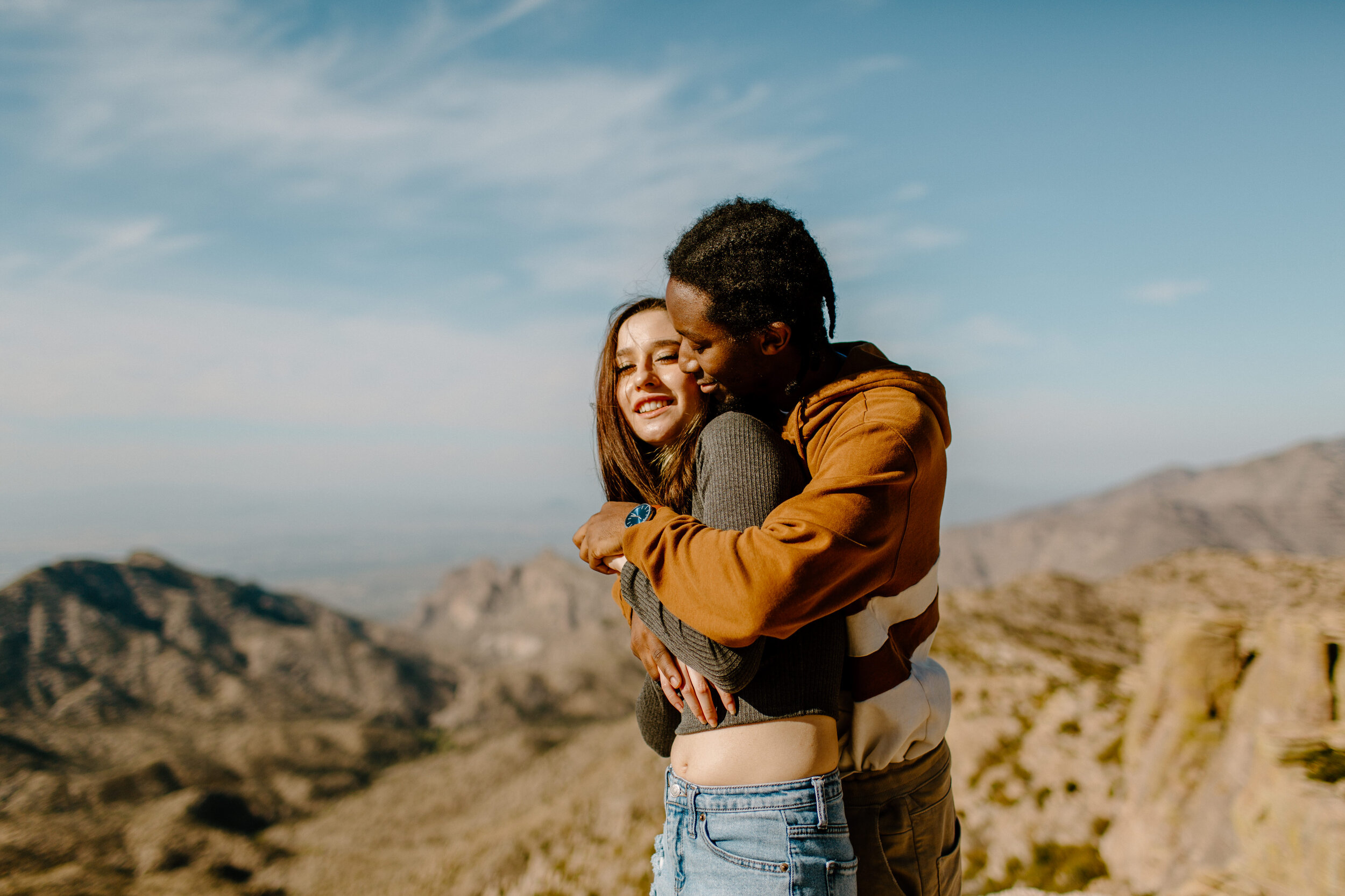  Man hugs his girlfriend from behind and kisses her neck at Windy Point on Mount Lemmon in Tucson Arizona. Arizona couples session, Lucy B. Photography. 