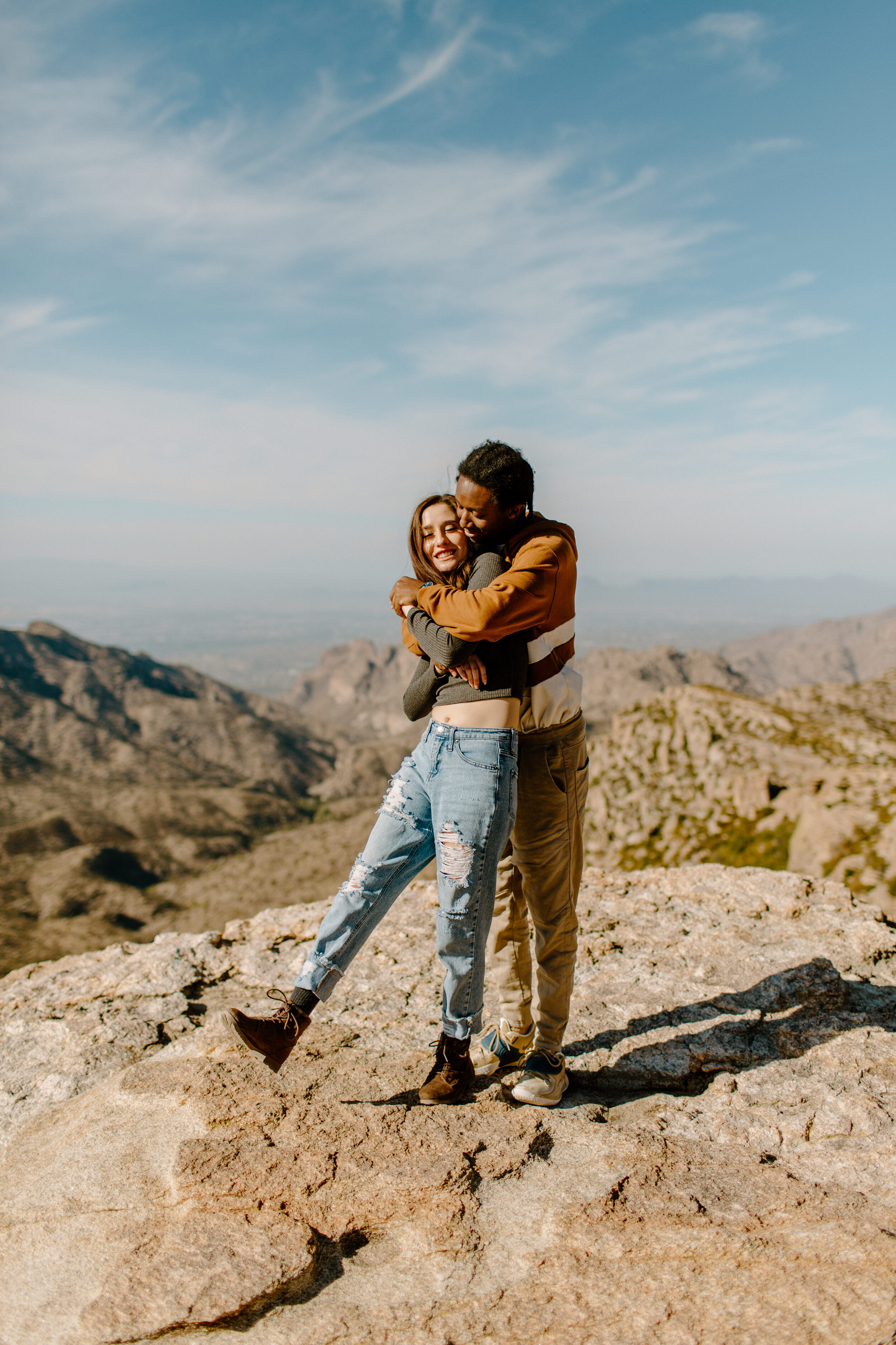  Man hugs his girlfriend from behind as she kicks her foot up at Windy Point on Mount Lemmon in Tucson Arizona. Tucson couples session, Lucy B. Photography. 