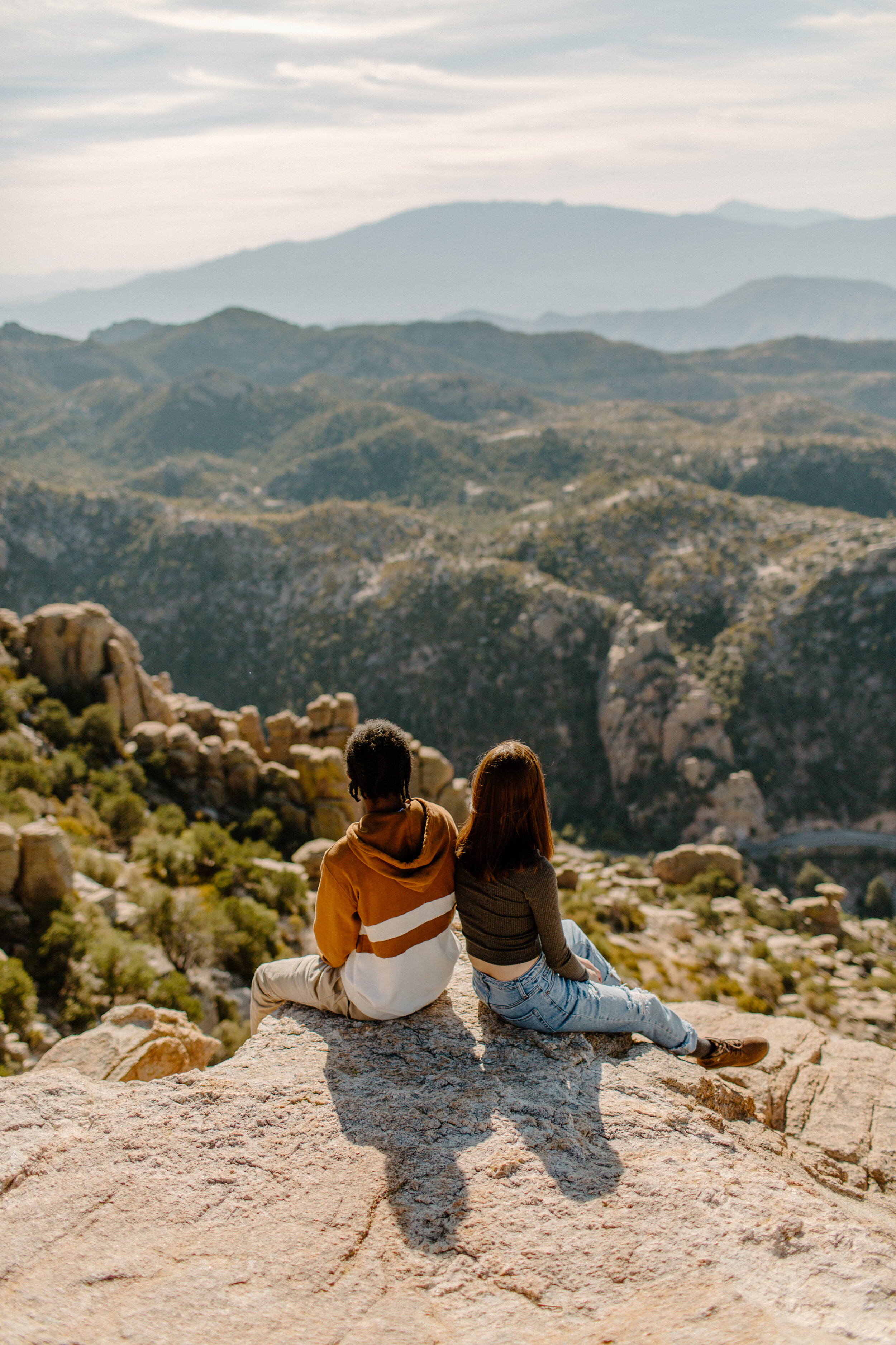  Couple sits back to back on a rock and looks out at the mountain view at Windy Point on Mount Lemmon in Tucson Arizona. Arizona couples session, Lucy B. Photography. 