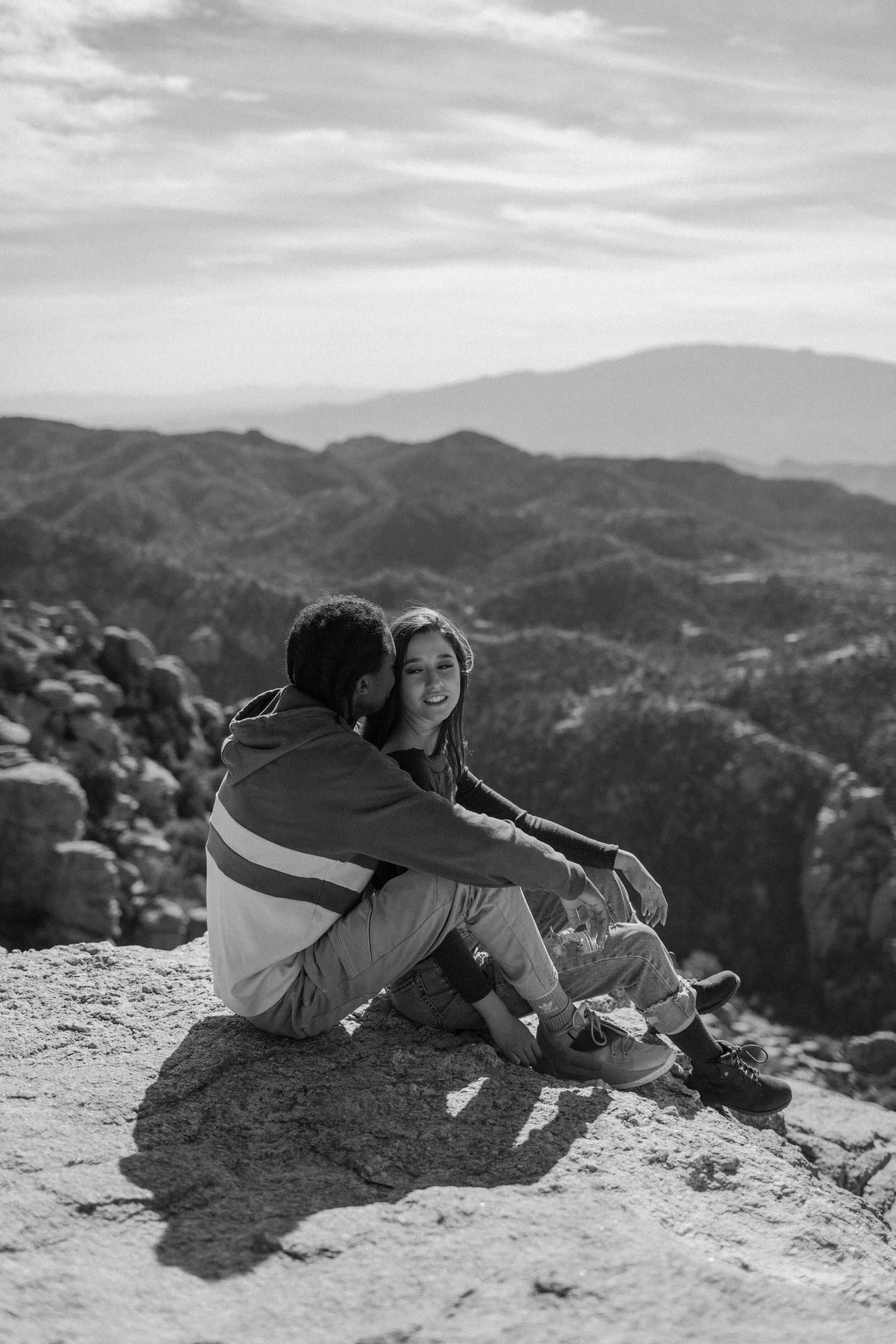  Black and white photo of a couple sitting and cuddling in front of a mountain view at Windy Point on Mount Lemmon in Tucson Arizona. Arizona couples photographer, Lucy B. Photography. 