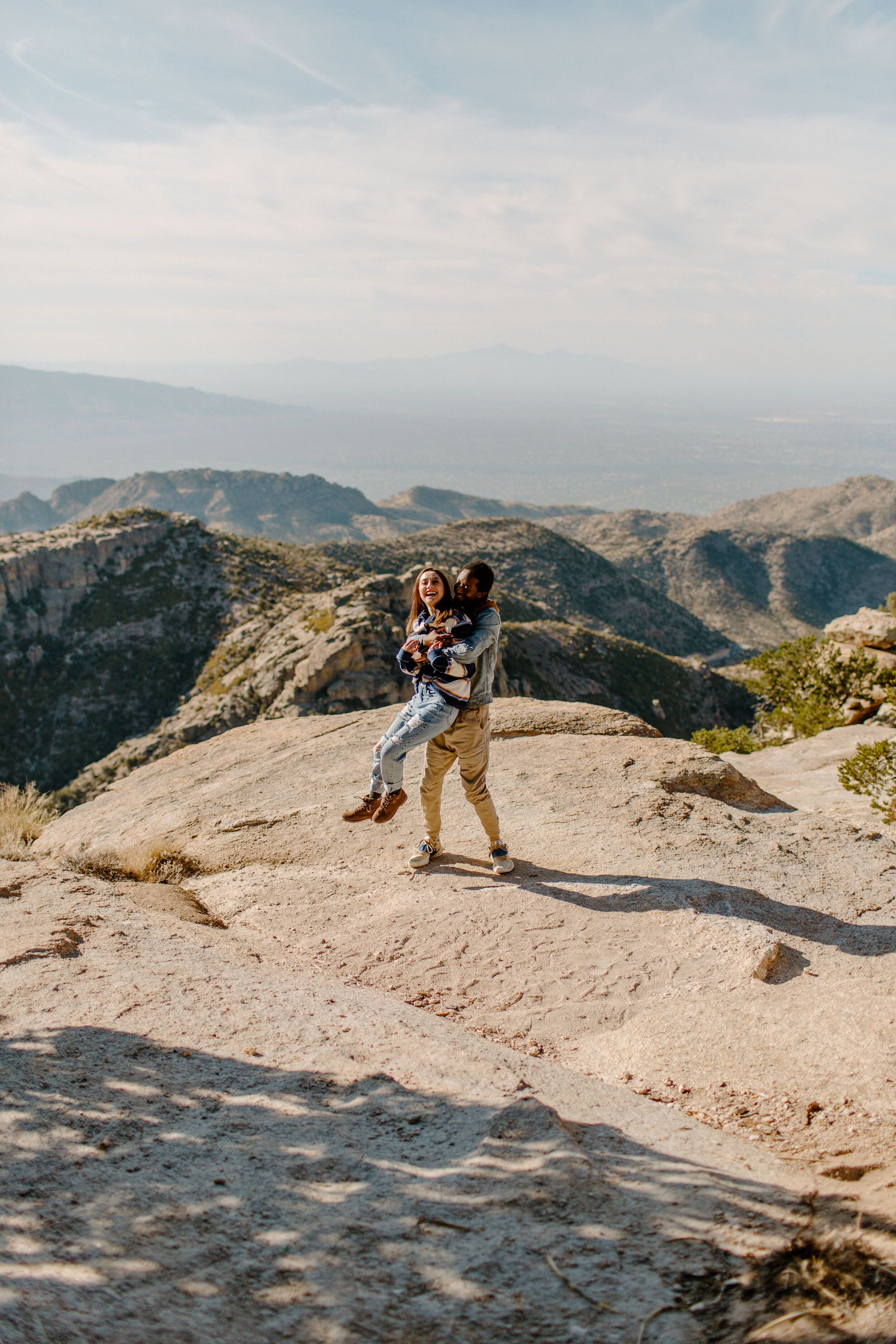  Boyfriend picks up his girlfriend and twirls her around and they both laugh at Windy Point on Mount Lemmon in Tucson Arizona. Arizona couples photographer, Lucy B. Photography. 