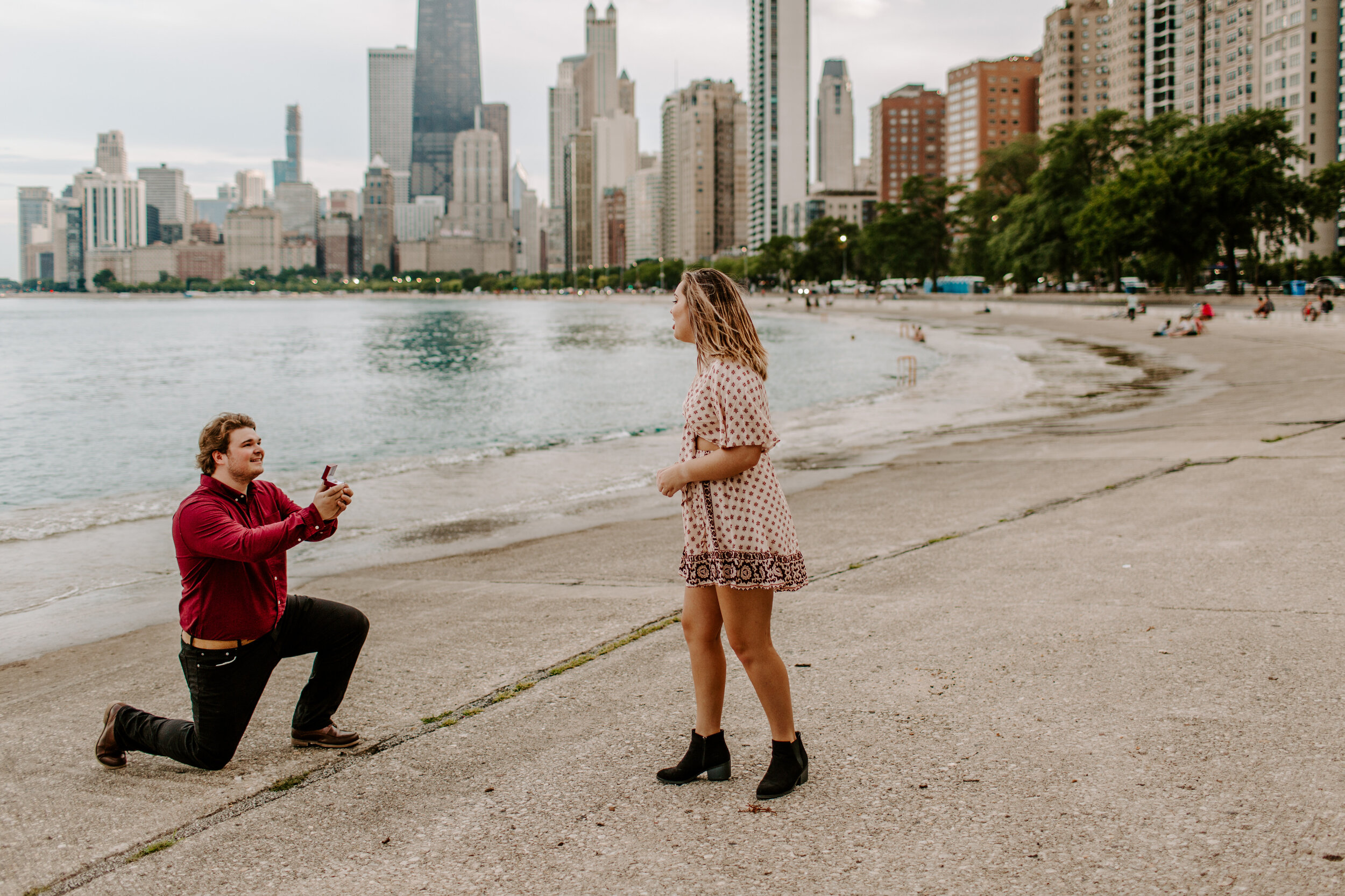  Surprise proposal at North Avenue Beach in Chicago, man proposes to his girlfriend by Lake Michigan in front of the Chicago skyline and she turns to see him. Lucy B. Photography. 