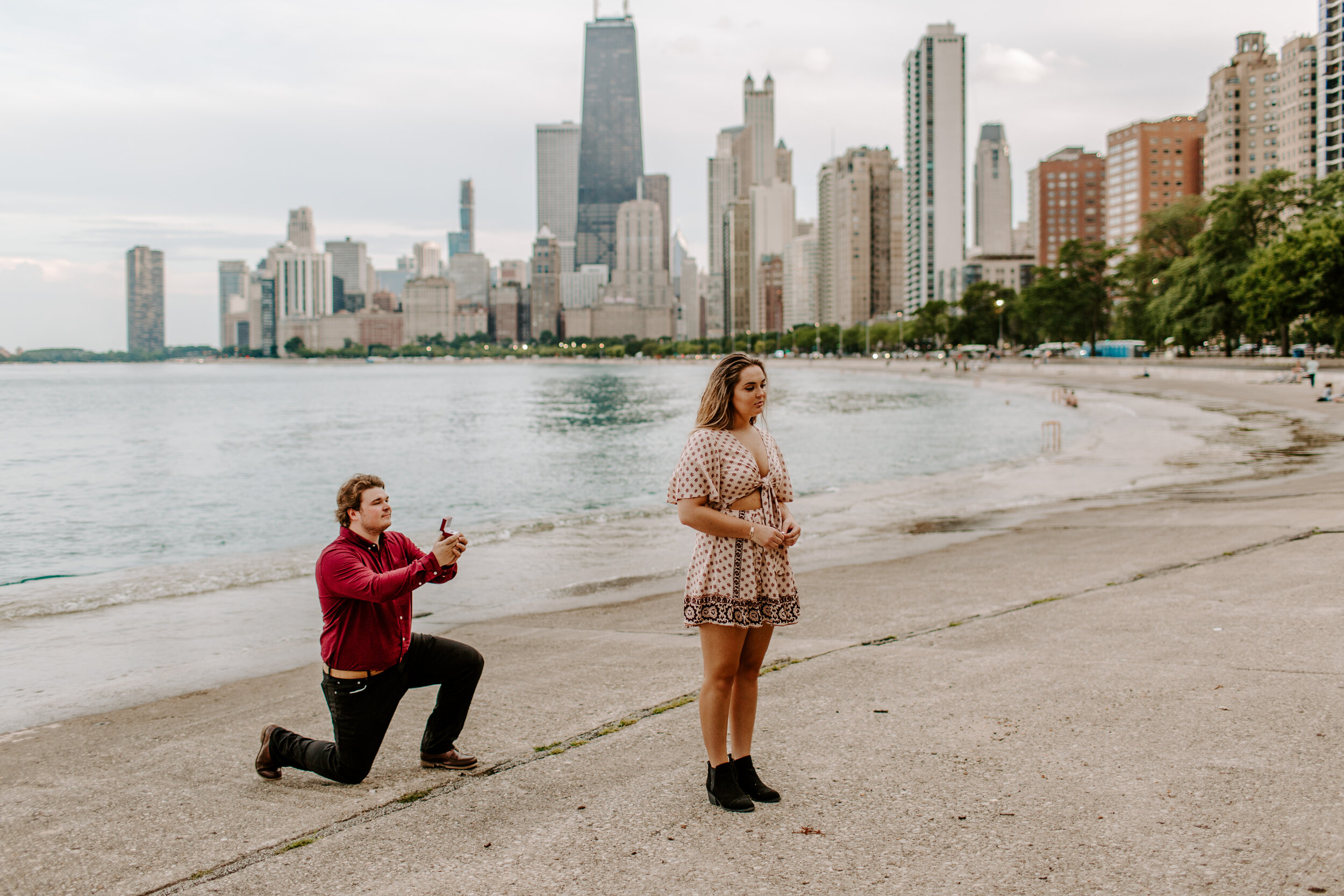  Surprise proposal at North Avenue Beach in Chicago, man proposes to his girlfriend by Lake Michigan in front of the Chicago skyline while her back is to him. Lucy B. Photography. 