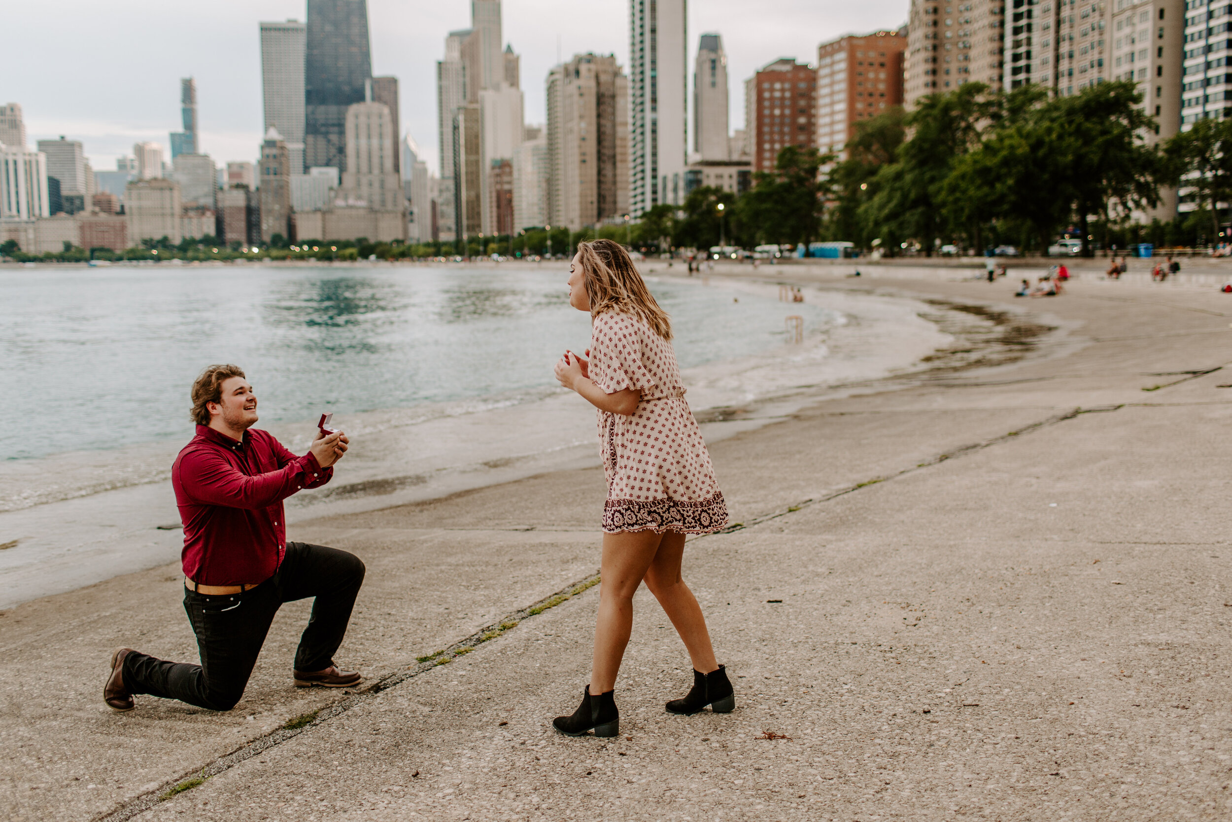  Surprise proposal at North Avenue Beach in Chicago, man proposes to his girlfriend by Lake Michigan in front of the Chicago skyline and she reacts happily. Lucy B. Photography. 