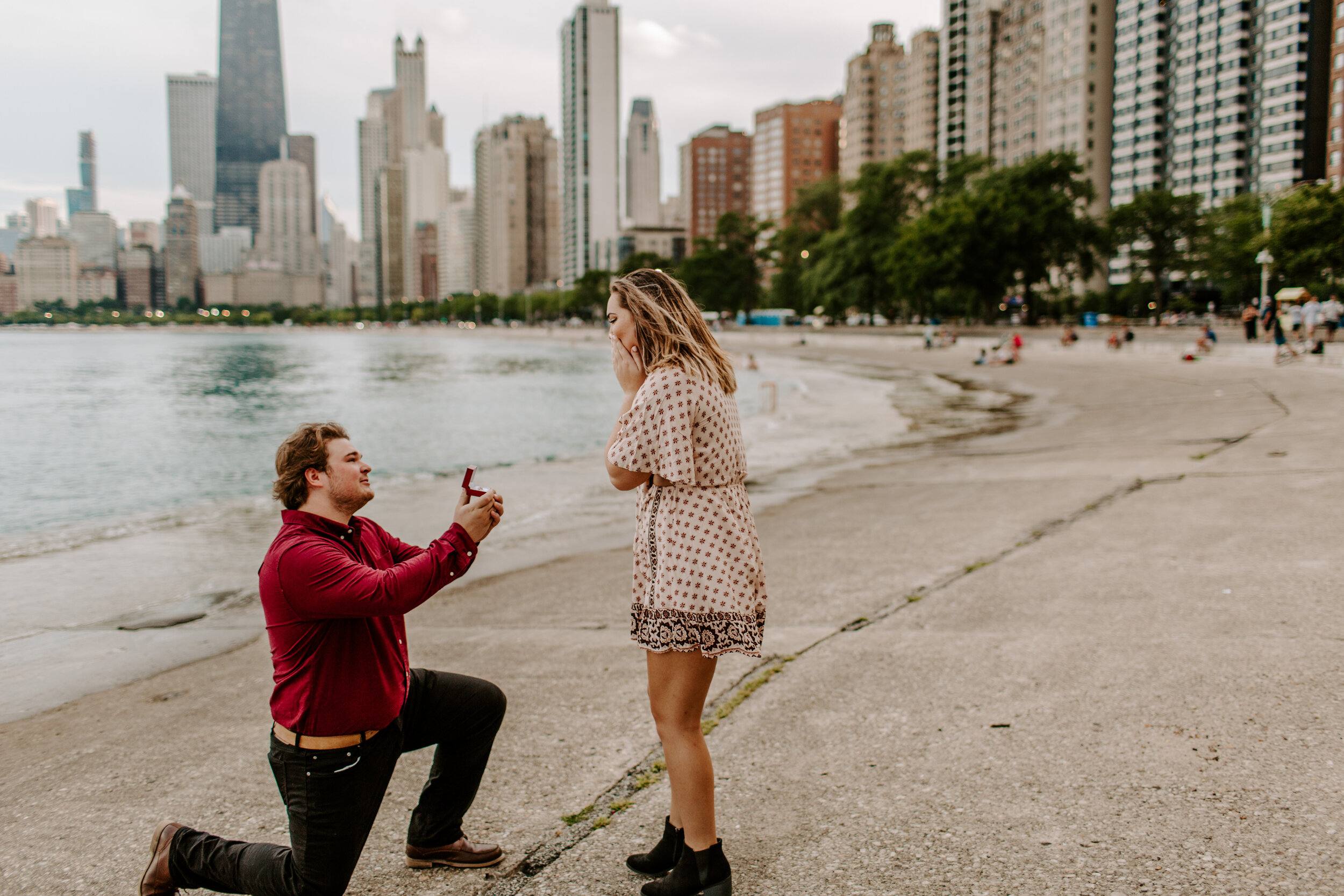  Surprise proposal at North Avenue Beach in Chicago, man proposes to his girlfriend by Lake Michigan in front of the Chicago skyline and she reacts emotionally. Lucy B. Photography. 