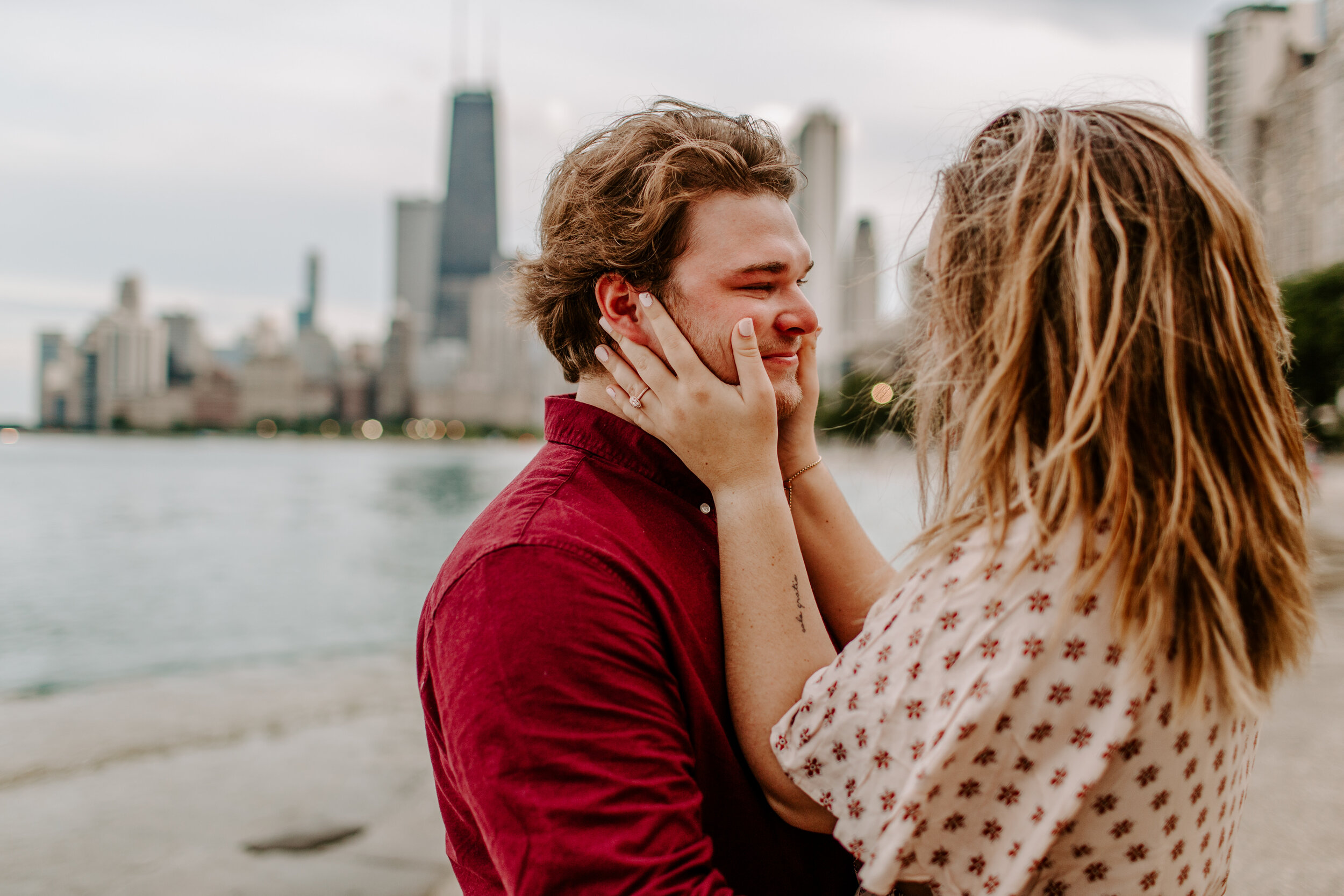  Surprise proposal at North Avenue Beach in Chicago next to Lake Michigan with the Chicago skyline in the back. Woman wears her new engagement ring and holds her fiancee’s face right after he did a surprise proposal, he has tears in his eyes. Lucy B.