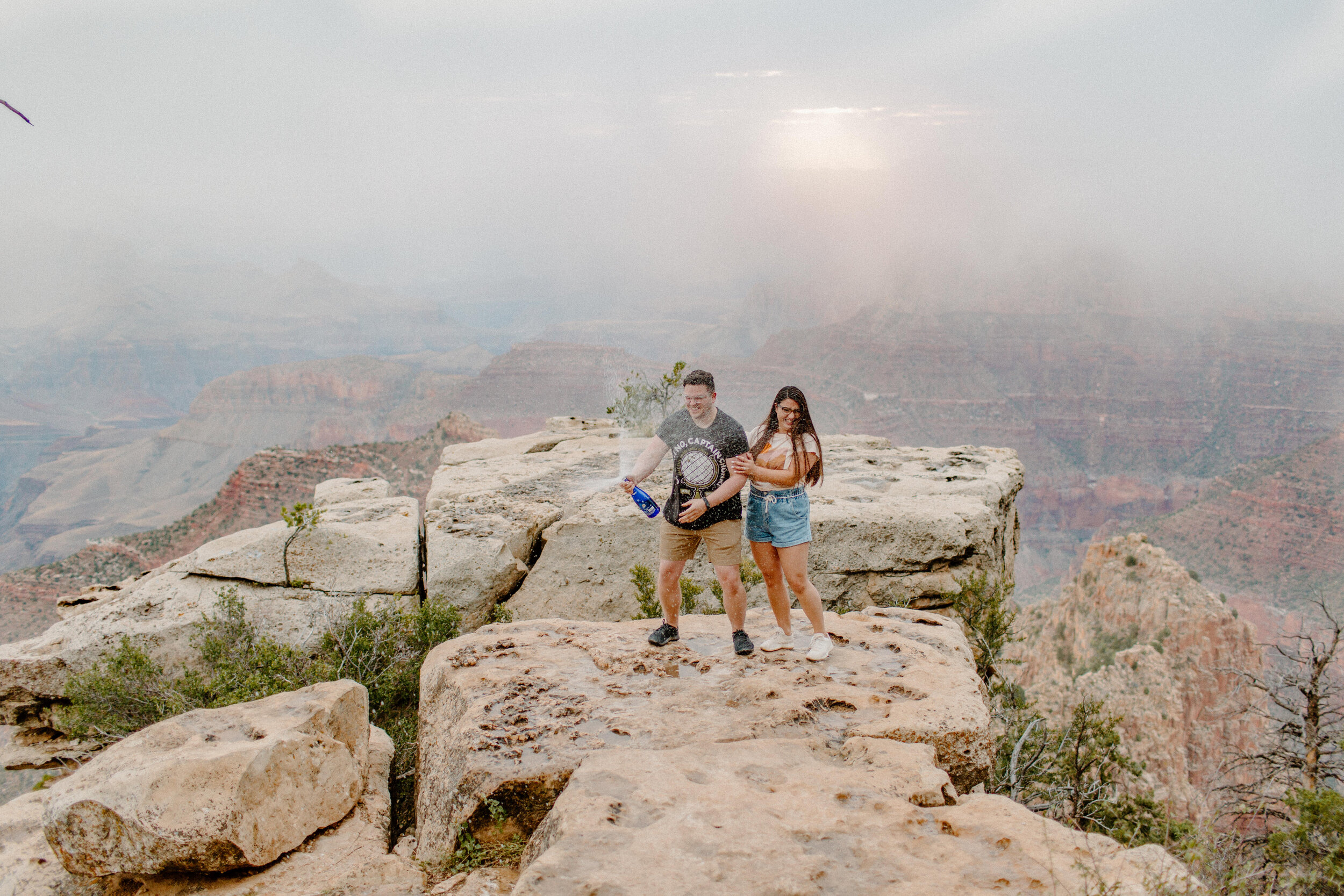  Surprise proposal at sunrise at the Grand Canyon South Rim, man and woman celebrate their new proposal by spraying a bottle of champagne while standing on the rim of the canyon. Grand Canyon engagement, Lucy B. Photography. 