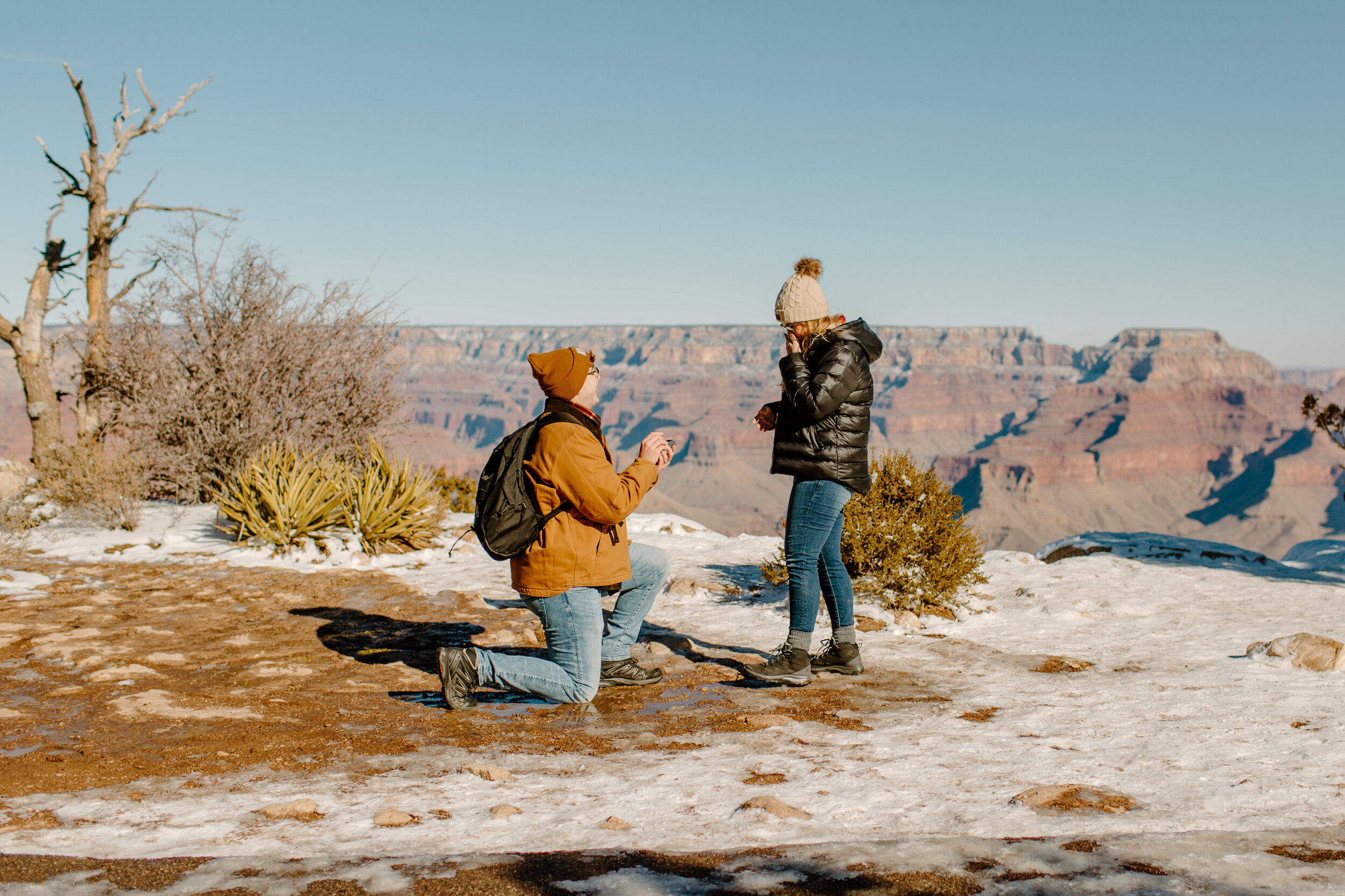  Surprise proposal at the Grand Canyon on the Rim Trail, man down on one knee proposing to his girlfriend at the rim of the Grand Canyon as she reacts happily. Grand Canyon engagement photographer, Grand Canyon proposal photographer, Lucy B. Photogra