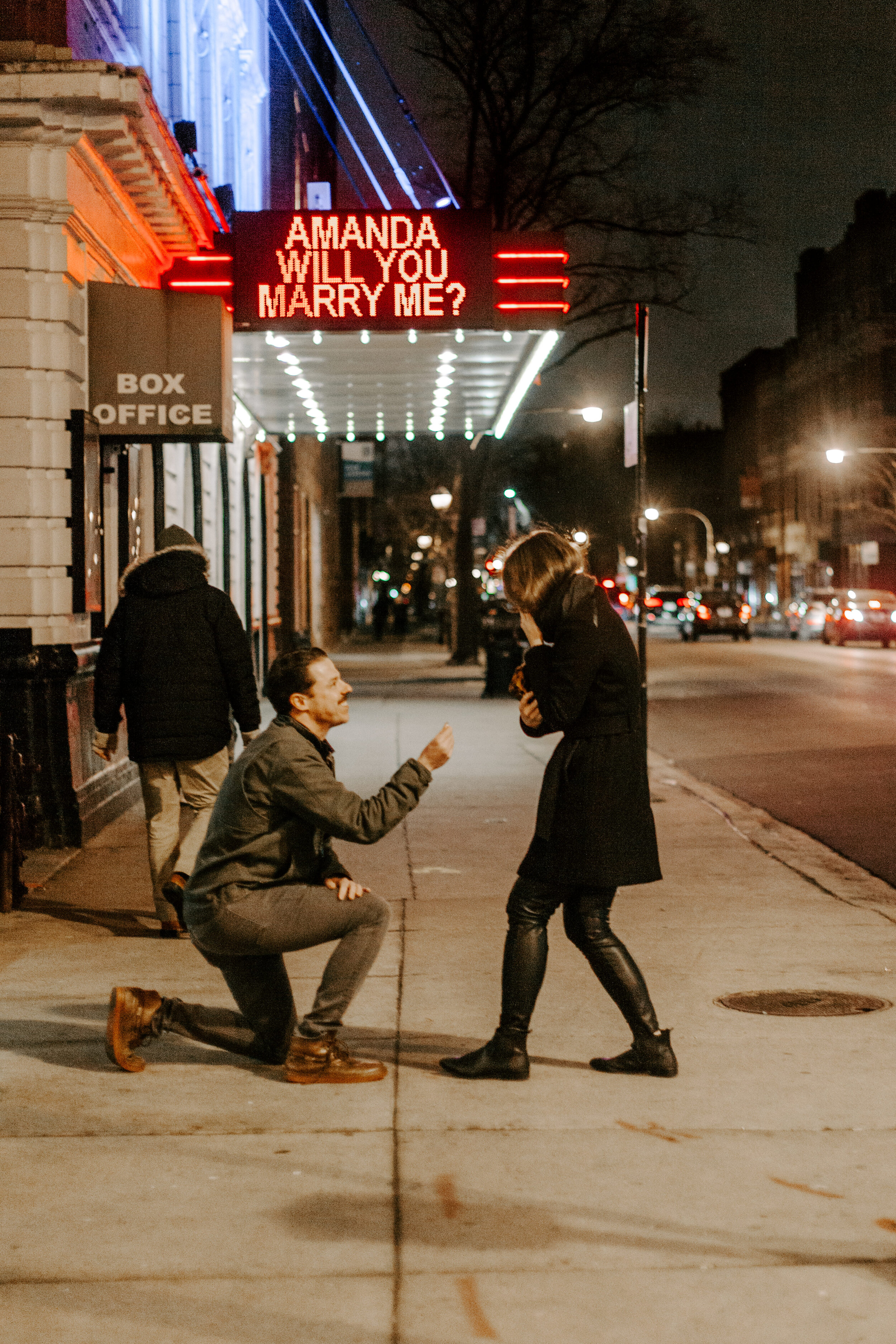  Chicago surprise proposal, woman reacts emotionally as her boyfriend proposes to her on one knee in front of theater marquee reading Amanda Will You Marry Me? Chicago engagement photographer, Lucy B. Photography 