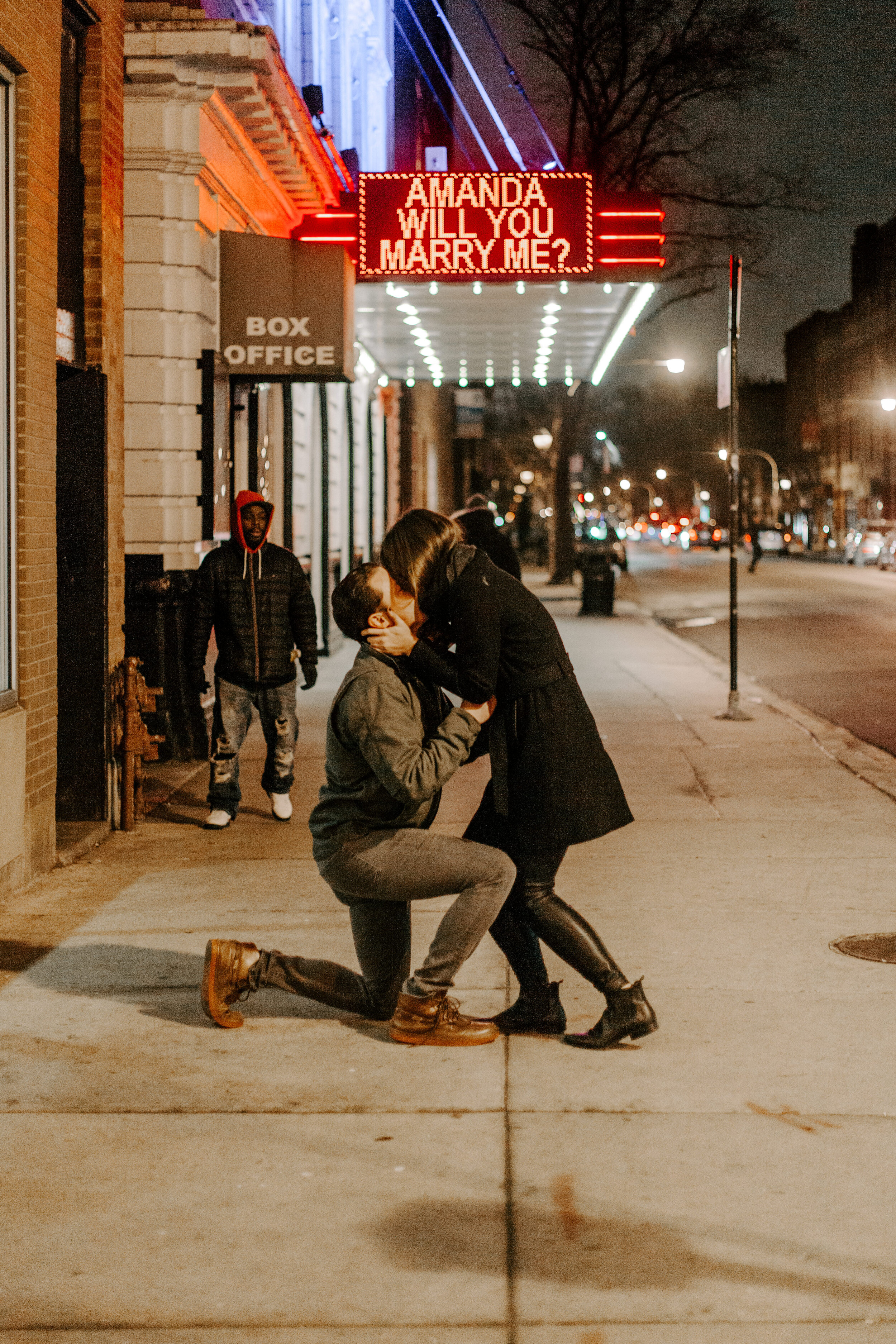  Chicago surprise proposal, woman leans down and kisses her boyfriend as he proposes in front of theater marquee reading Amanda Will You Marry Me? Chicago engagement photographer, Lucy B. Photography 
