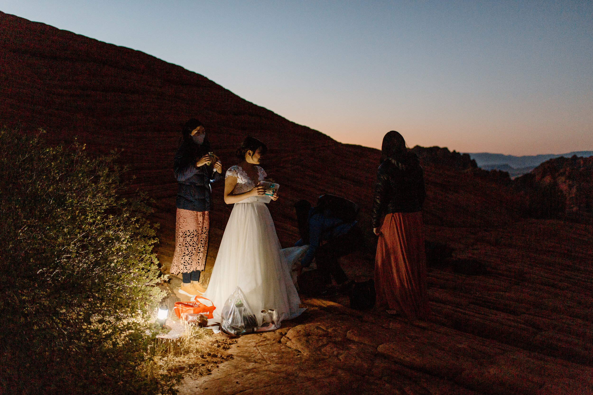  Bride gets ready by flashlight for her Utah elopement as the sun starts to rise in the background at Snow Canyon State Park in St. George Utah. Utah elppement photographer, Lucy B. Photography. 
