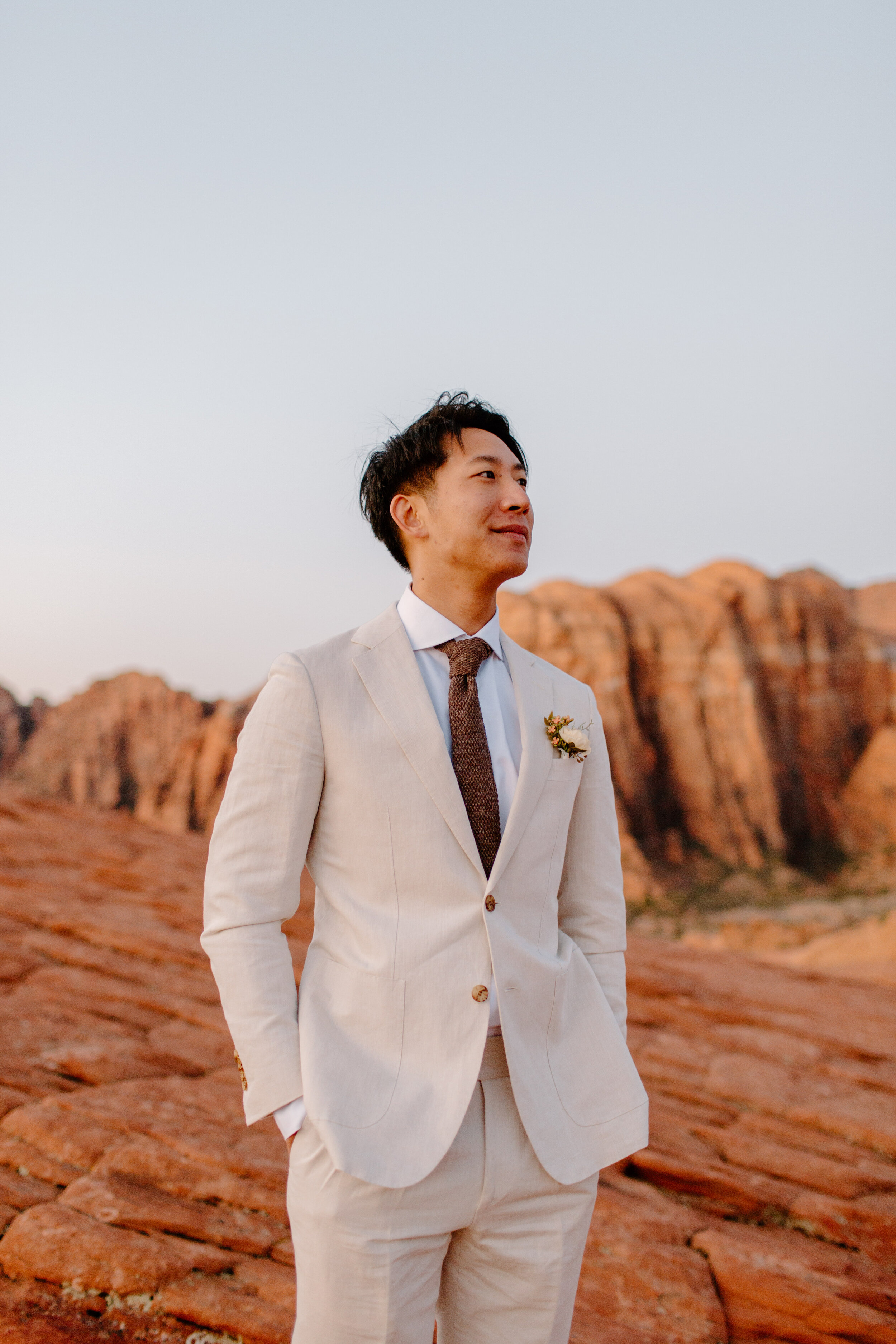  Groom stands in front of red rocks at Snow Canyon State Park in St. George Utah. Utah elopement photographer, Lucy B. Photography. 