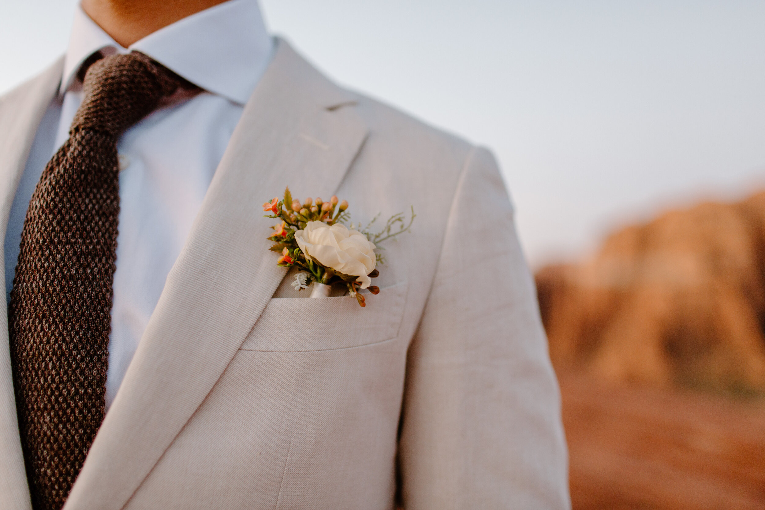  Close up photo of groom’s boutonniere in the pocket of his white suit at Snow Canyon State Park in St. George Utah. Utah elopement photographer, Lucy B. Photography. 